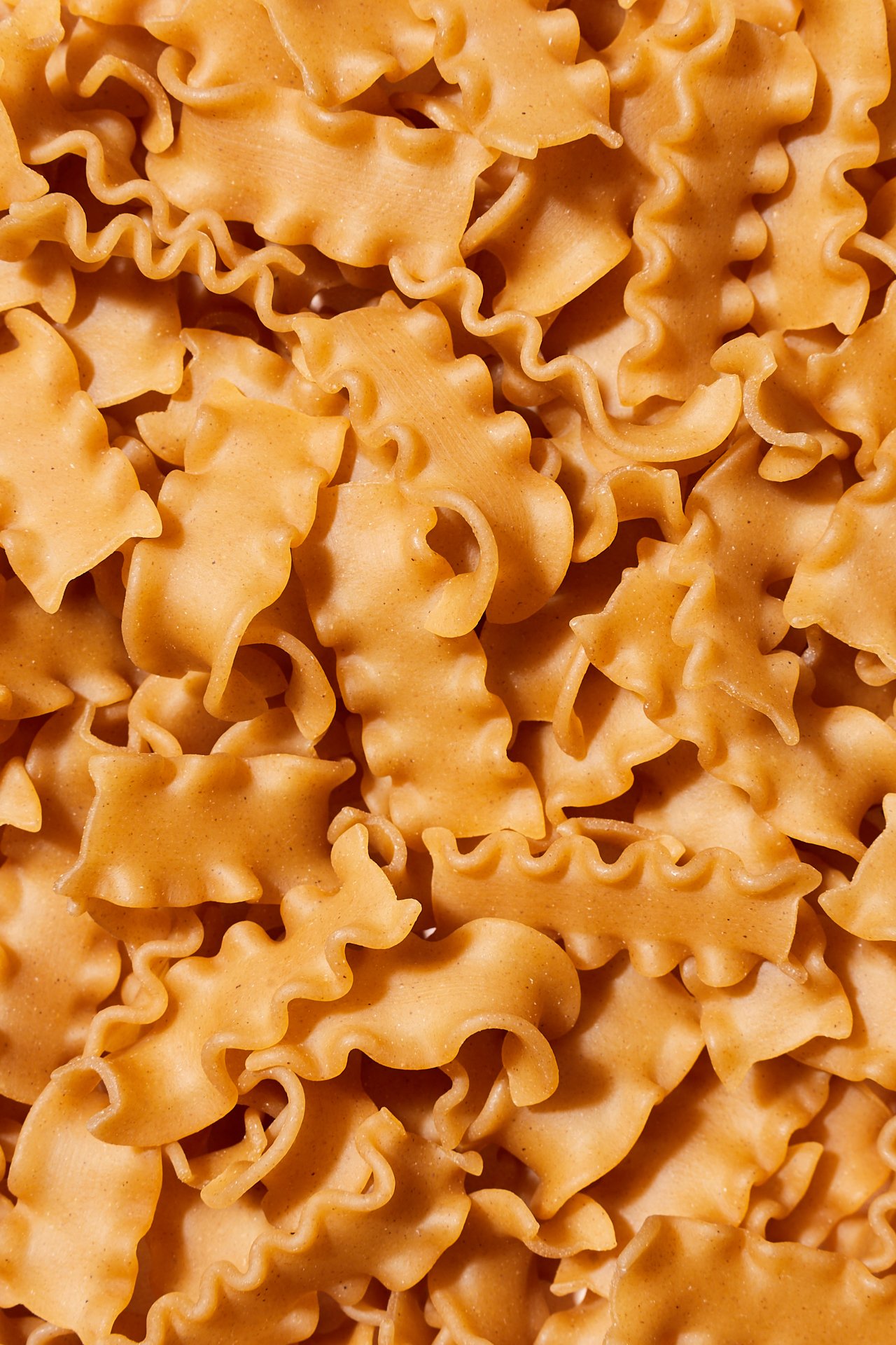 Close-up of uncooked orange pasta, including farfalle, rotini, and fusilli shapes.