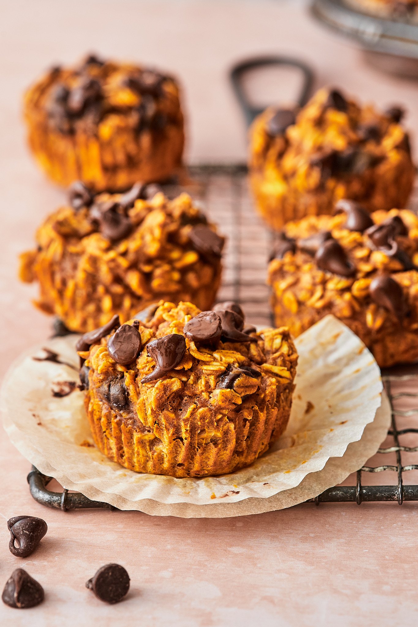 Close-up of chocolate chip and oatmeal muffins on a wire cooling rack, with one muffin on a paper liner in the foreground.