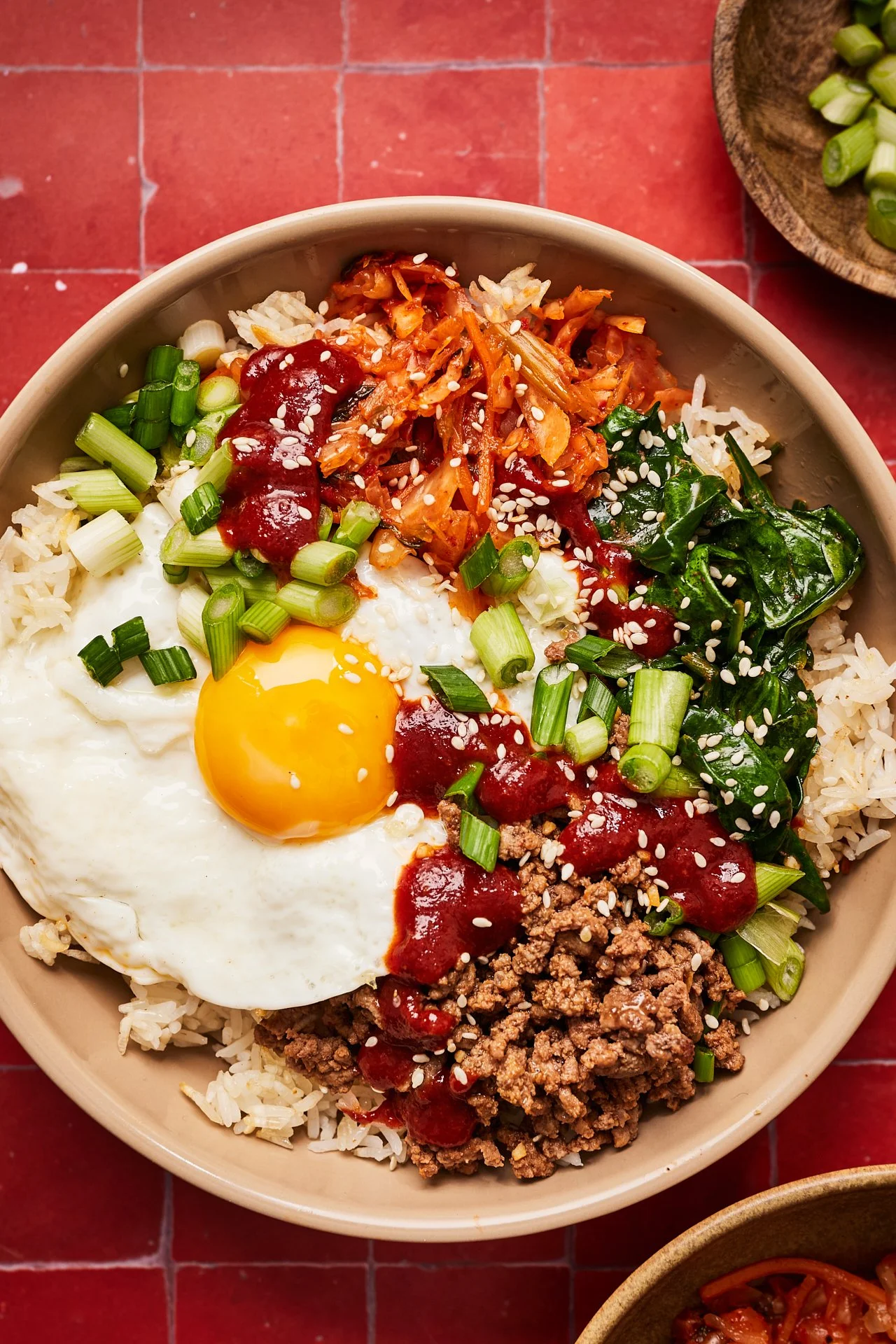 Bowl of rice topped with a fried egg, ground meat, spinach, chopped green onions, kimchi, kimchi-flavored sauce, and sesame seeds.