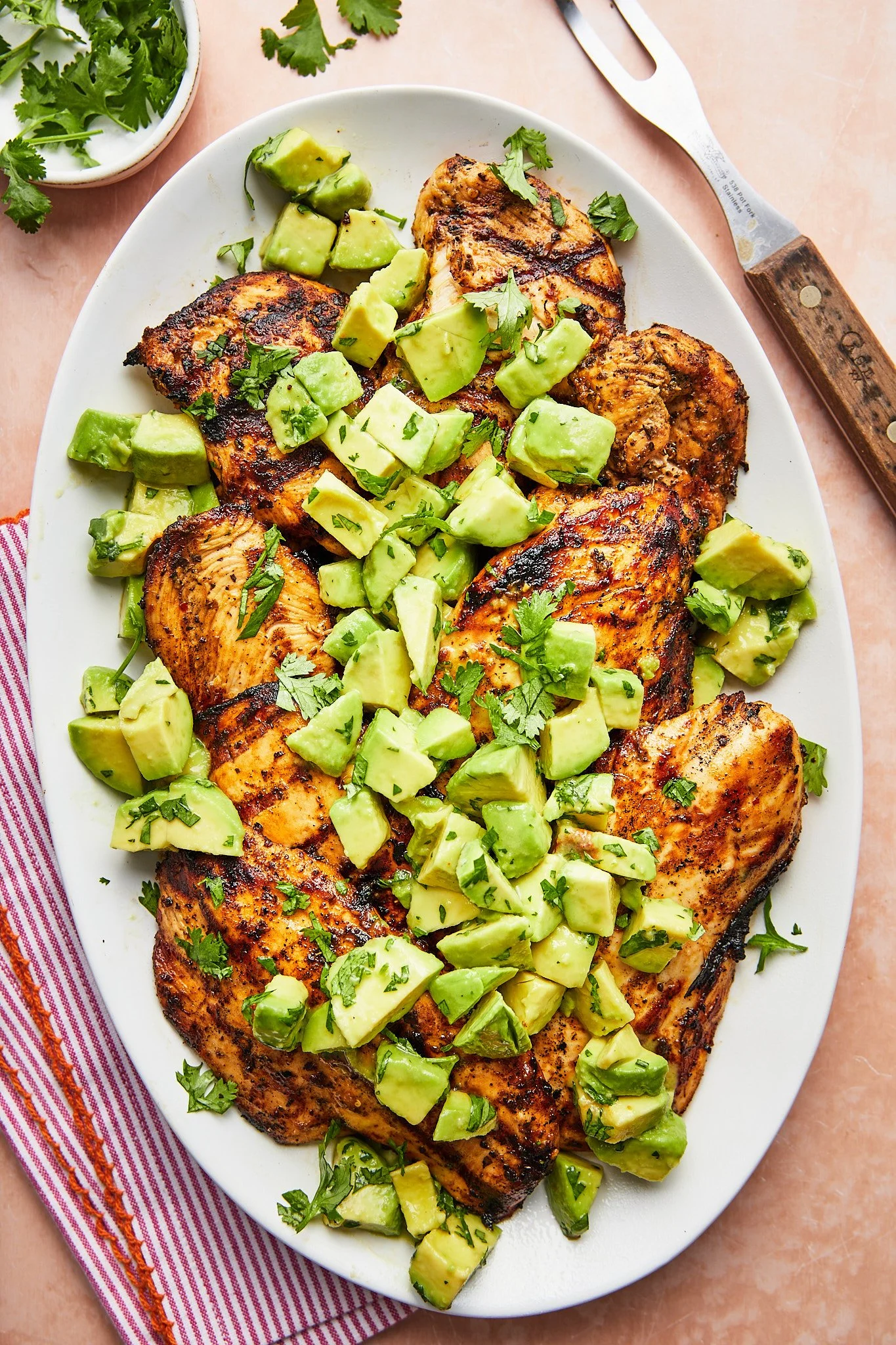 Grilled salmon fillets topped with chopped avocado and herbs on a white oval plate.