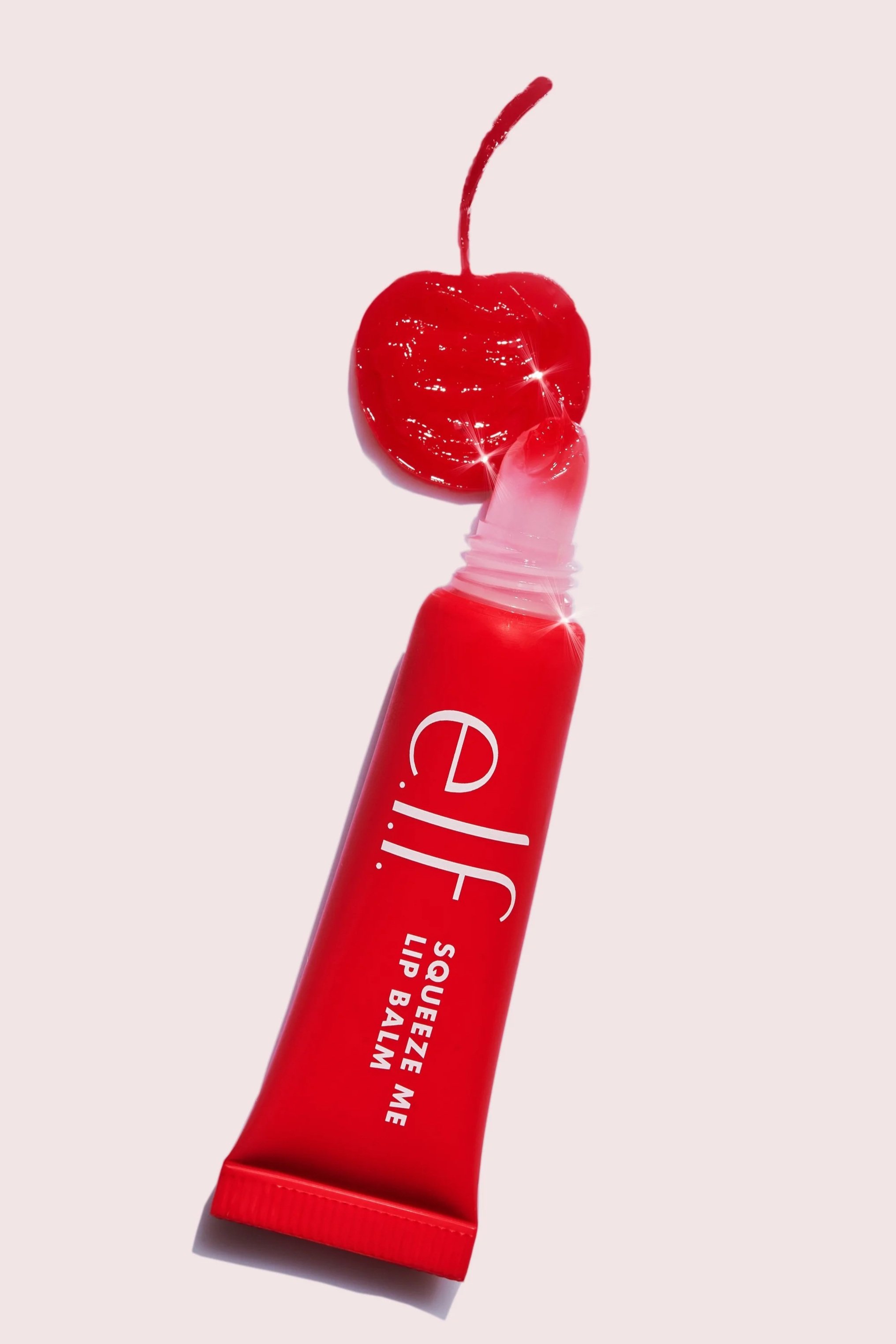 A red squeeze lip balm tube with a cherry on top, against a light pink background.