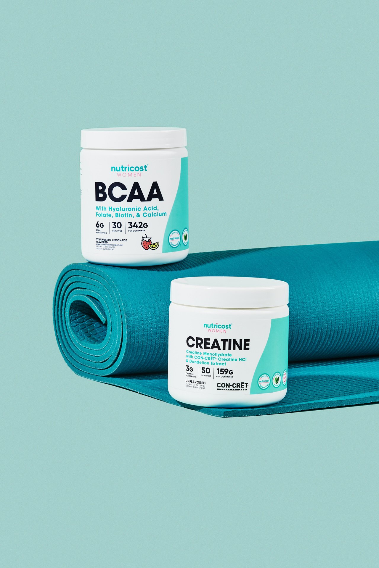 Containers of Nutricost BCAA and Creatine supplements placed on a rolled-up blue yoga mat against a light green background.