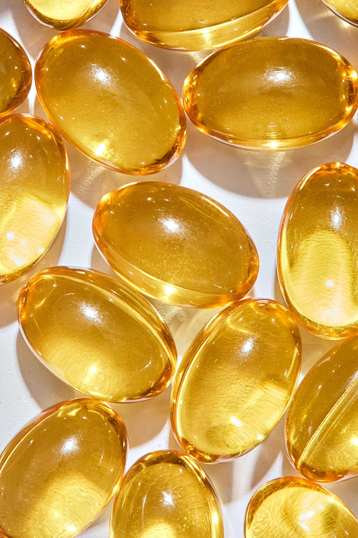 Close-up of multiple translucent yellow oval capsules or gel pills arranged on a white surface.