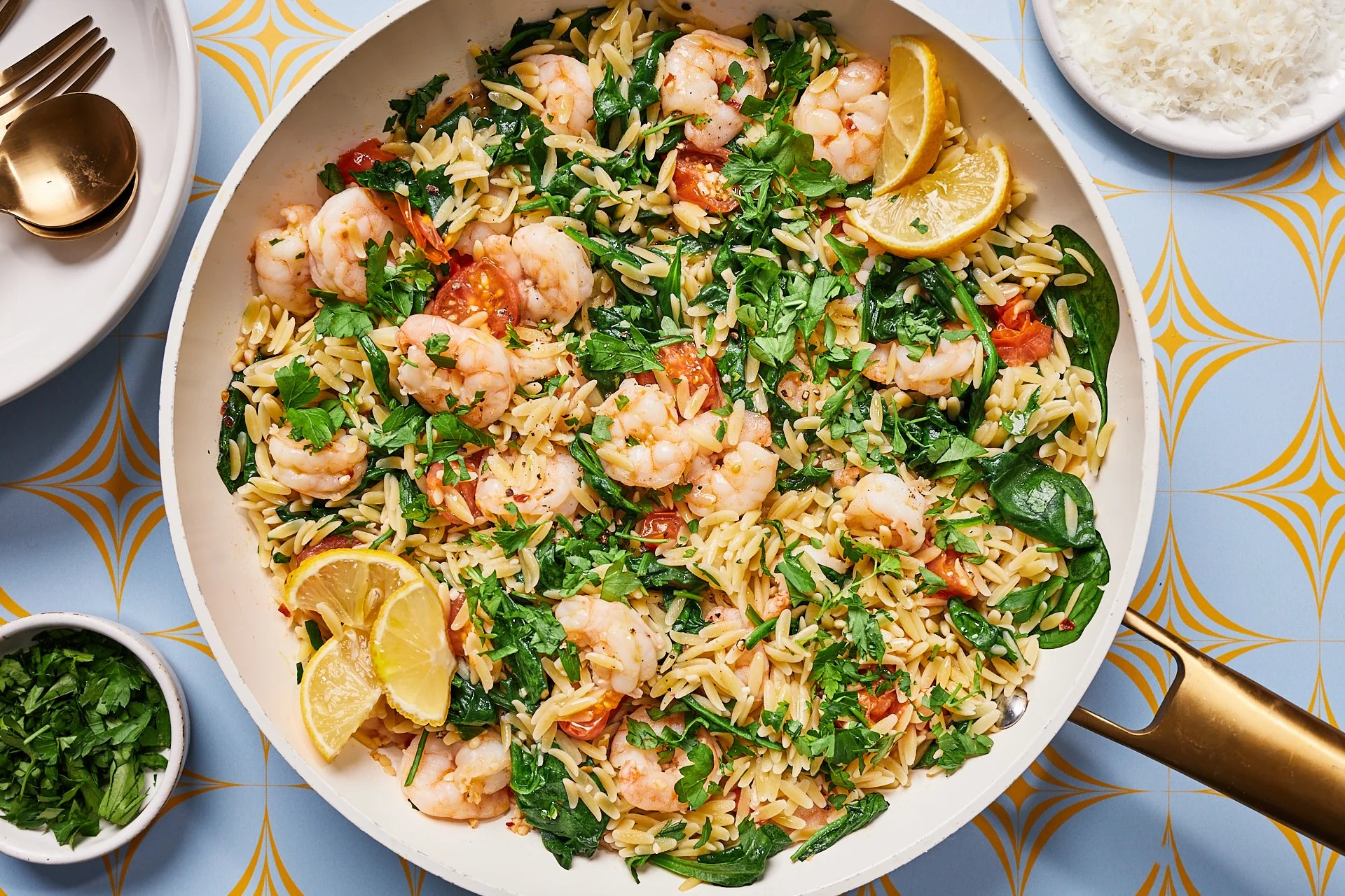 Shrimp and orzo pasta with cherry tomatoes, spinach, and parsley, garnished with lemon wedges and served in a white pan.