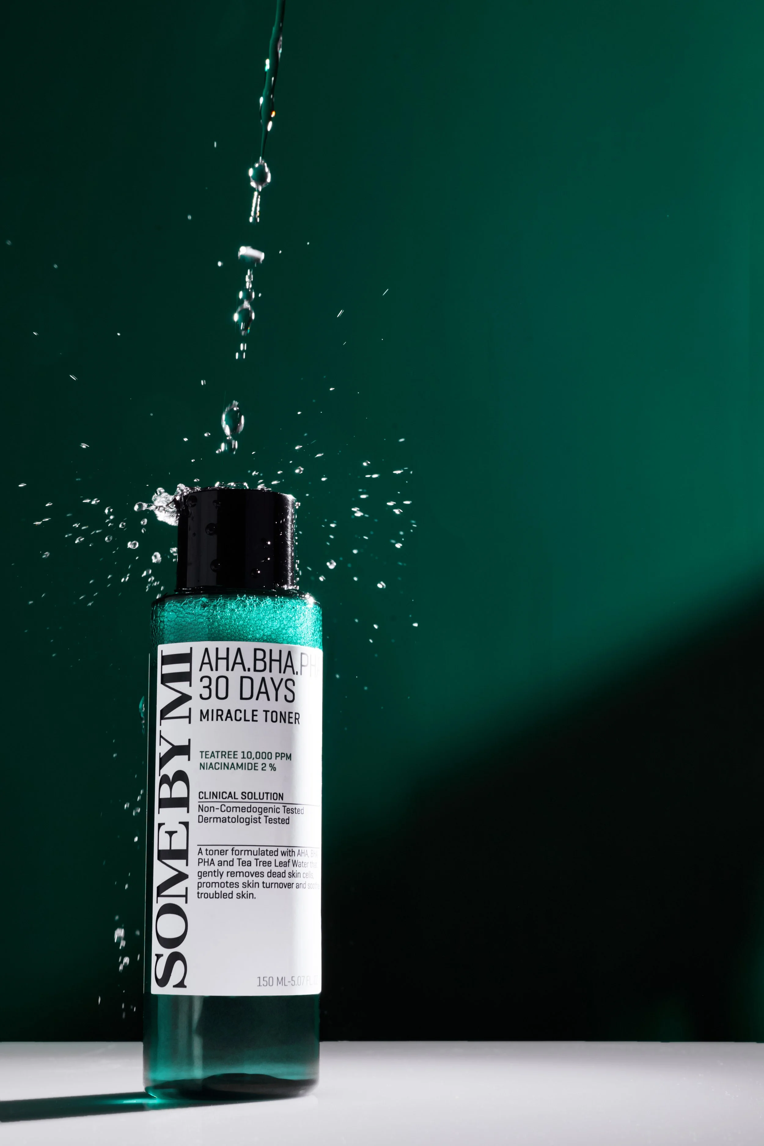 A bottle of SoBeYMI AHA BHA 30 Days Miracle Toner with water droplets splashing around it, set against a dark green background.