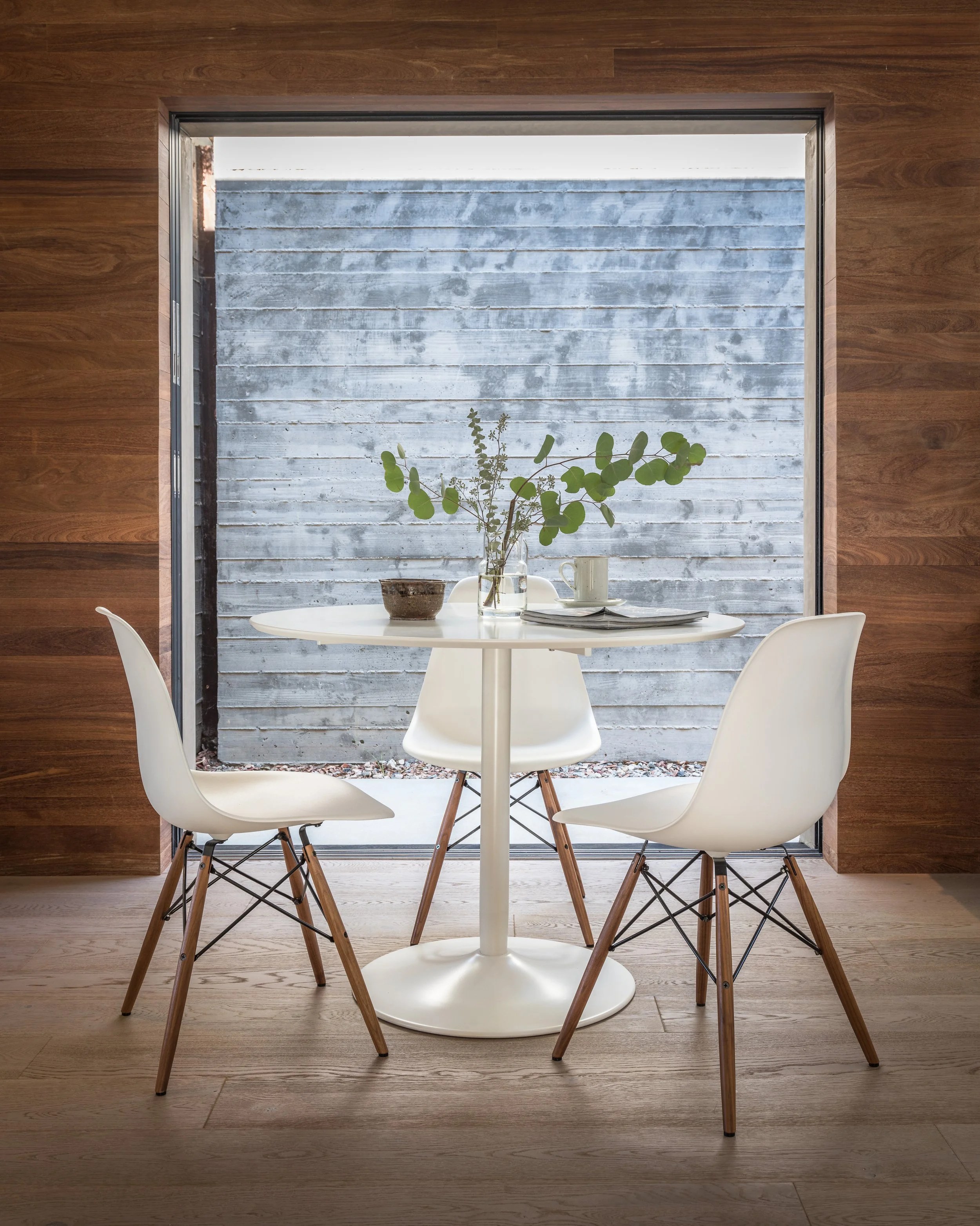 Minimalist dining setup with white table, chairs, and green plant