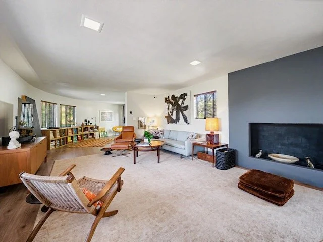 Spacious living room with modern furniture, a large abstract wall art, a fireplace, and multiple windows allowing natural light.