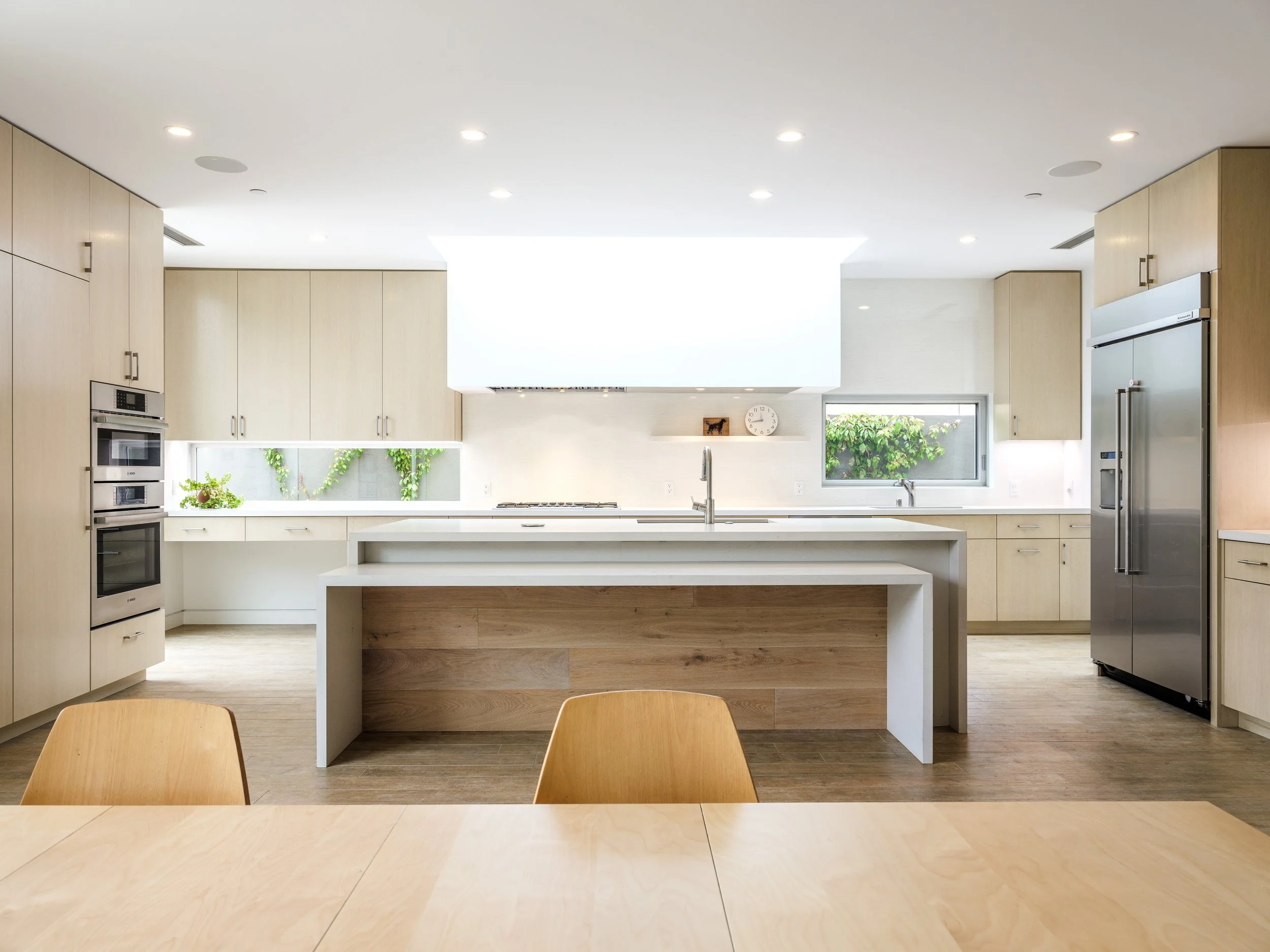 Modern kitchen with wooden cabinetry, stainless steel appliances, island with sink, and dining table.