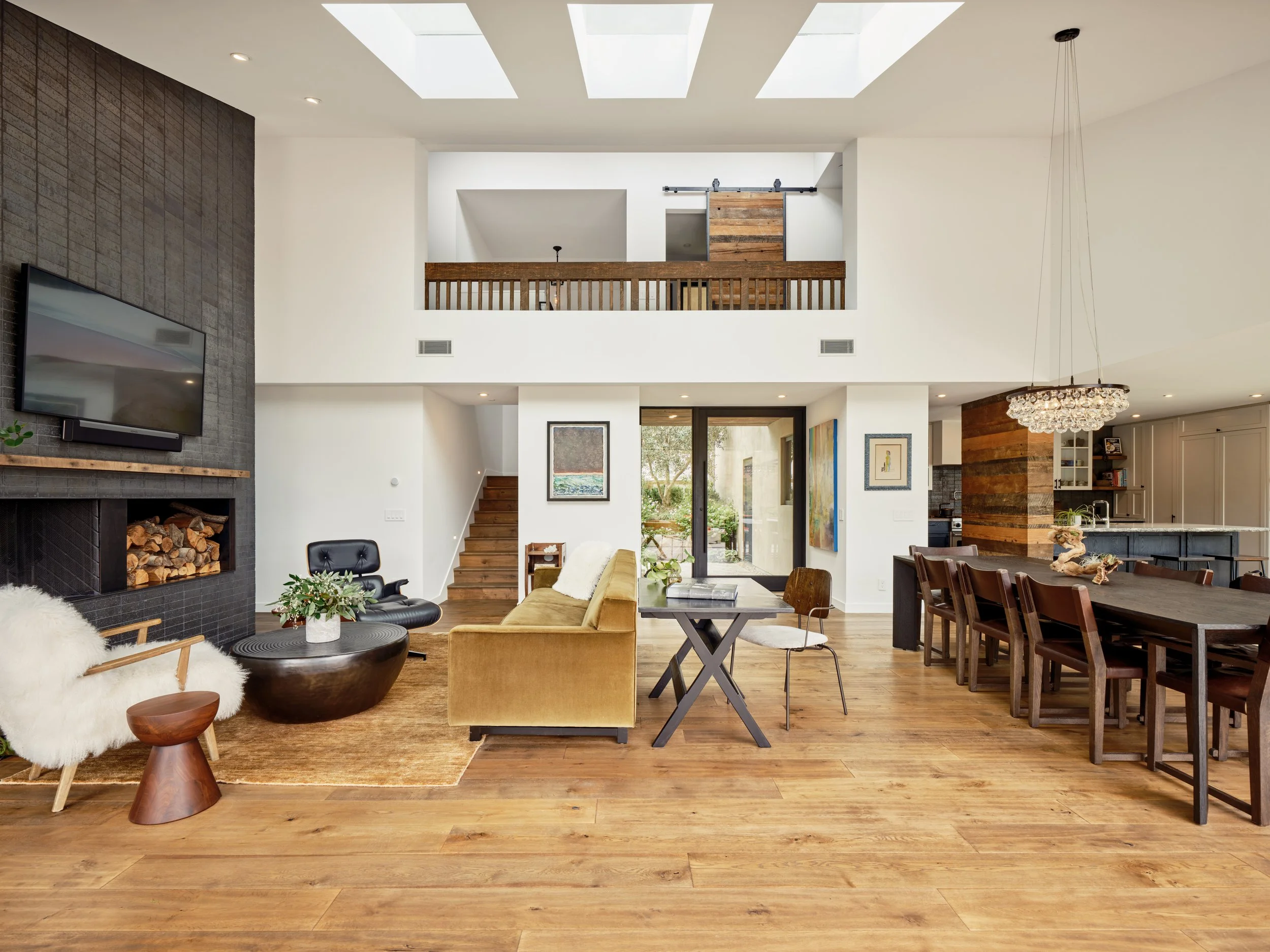 Modern open-concept living and dining area with wooden floors, skylights, a fireplace, and contemporary furnishings.