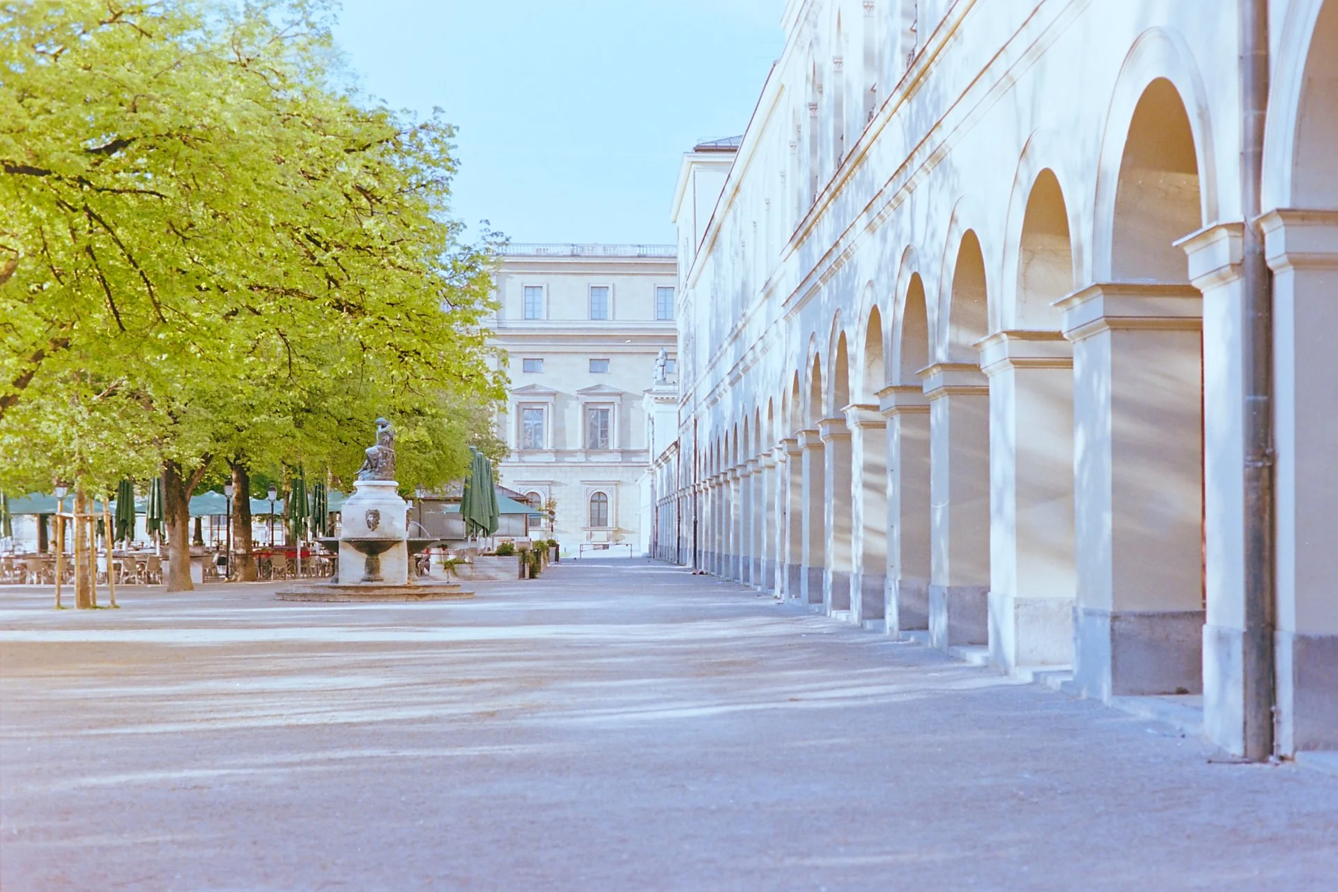 pring pathway in Munich’s Hofgarten with the Residenz in the background, sunlit trees on the left, and arcades on the right, shot on 35mm film.