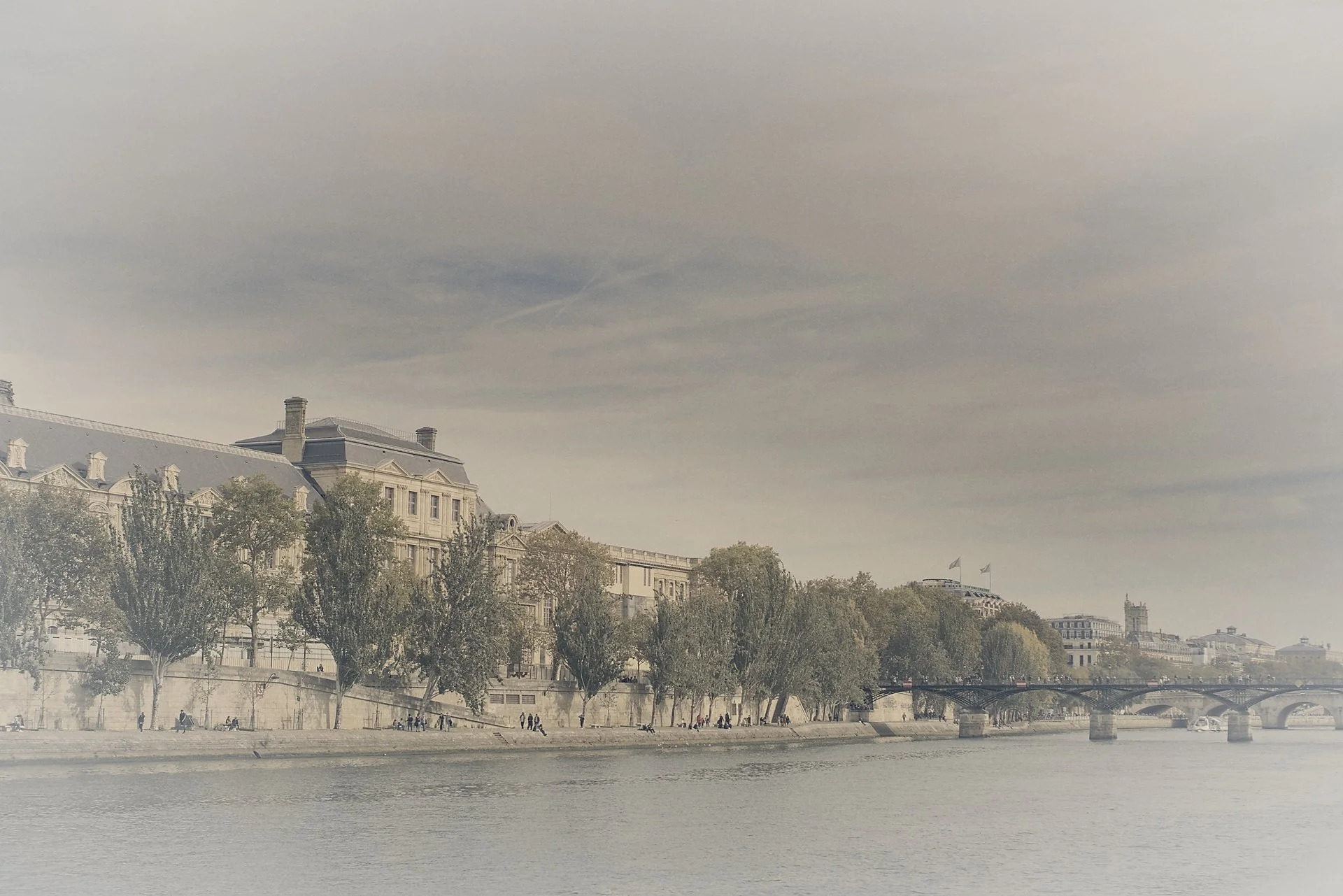 Limited‑edition waterside view of the Louvre along Quai François‑Mitterrand with the Pont des Arts in the distance.
