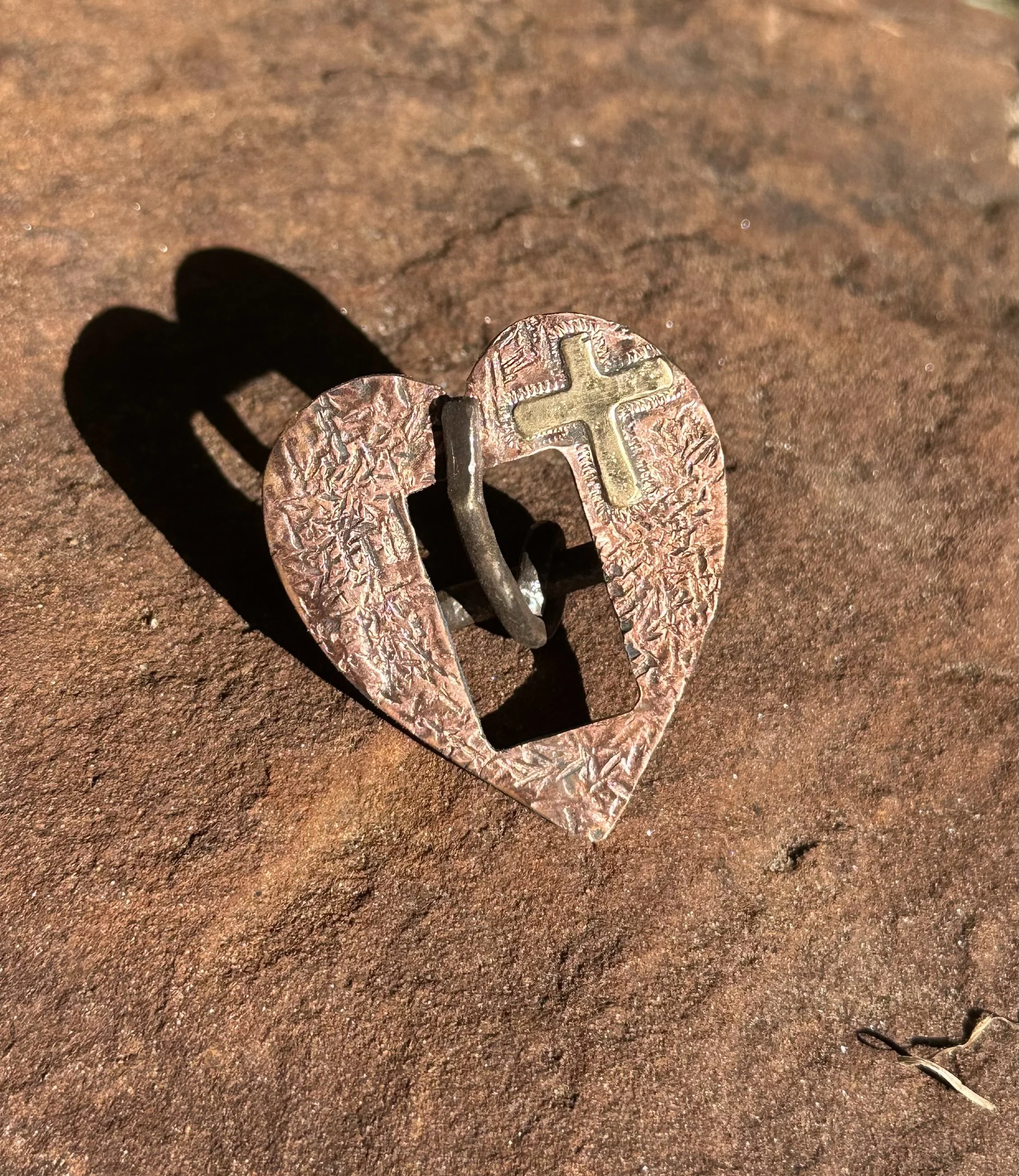 Textured copper plated heart shaped buckle with a brass cross in the top right