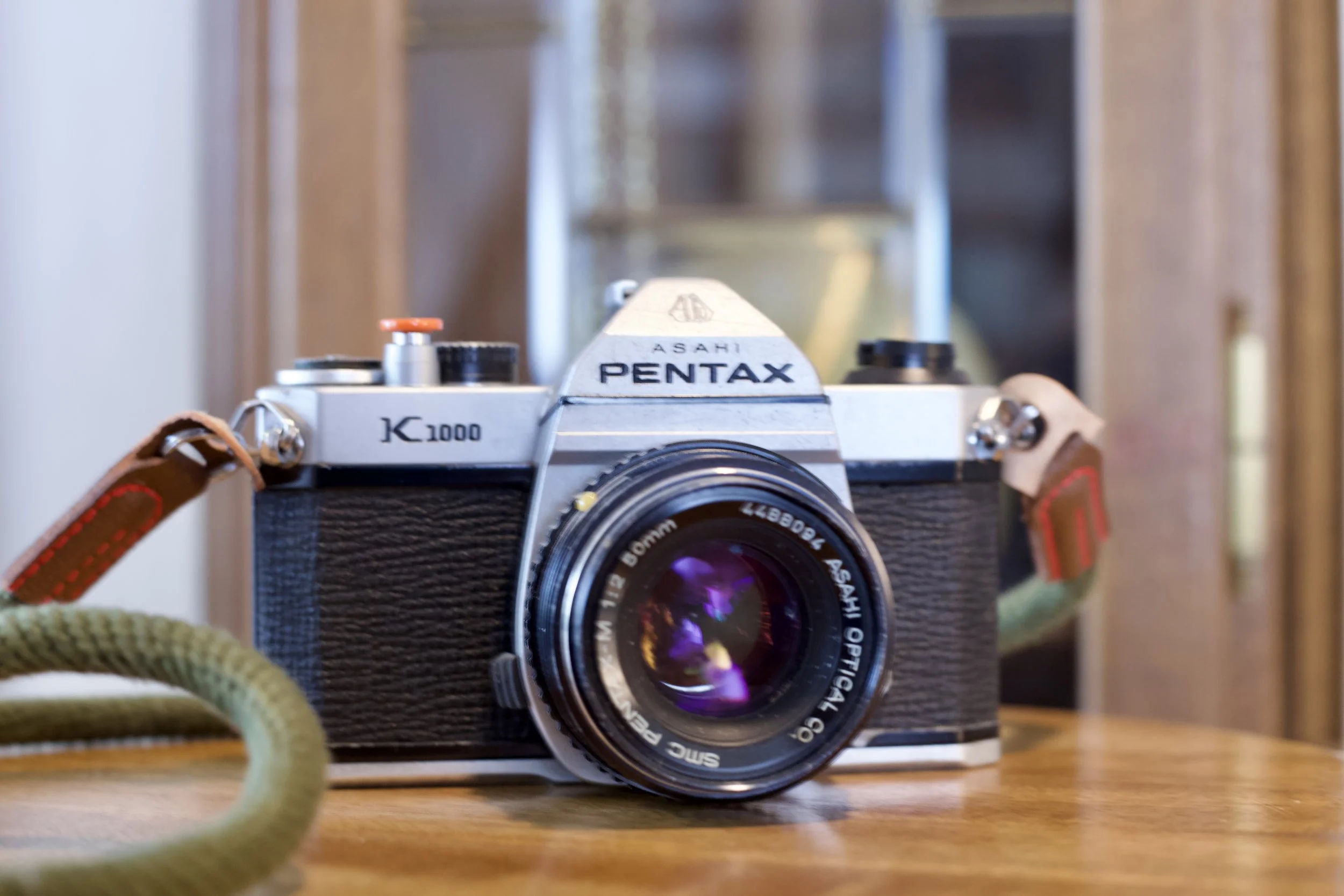 Pentax K1000 film camera with lens and strap on a wooden surface.