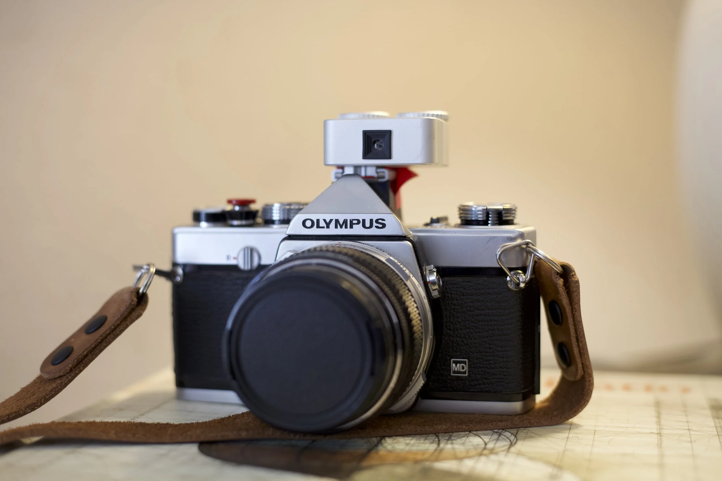Vintage Olympus film camera with a leather strap on a table.
