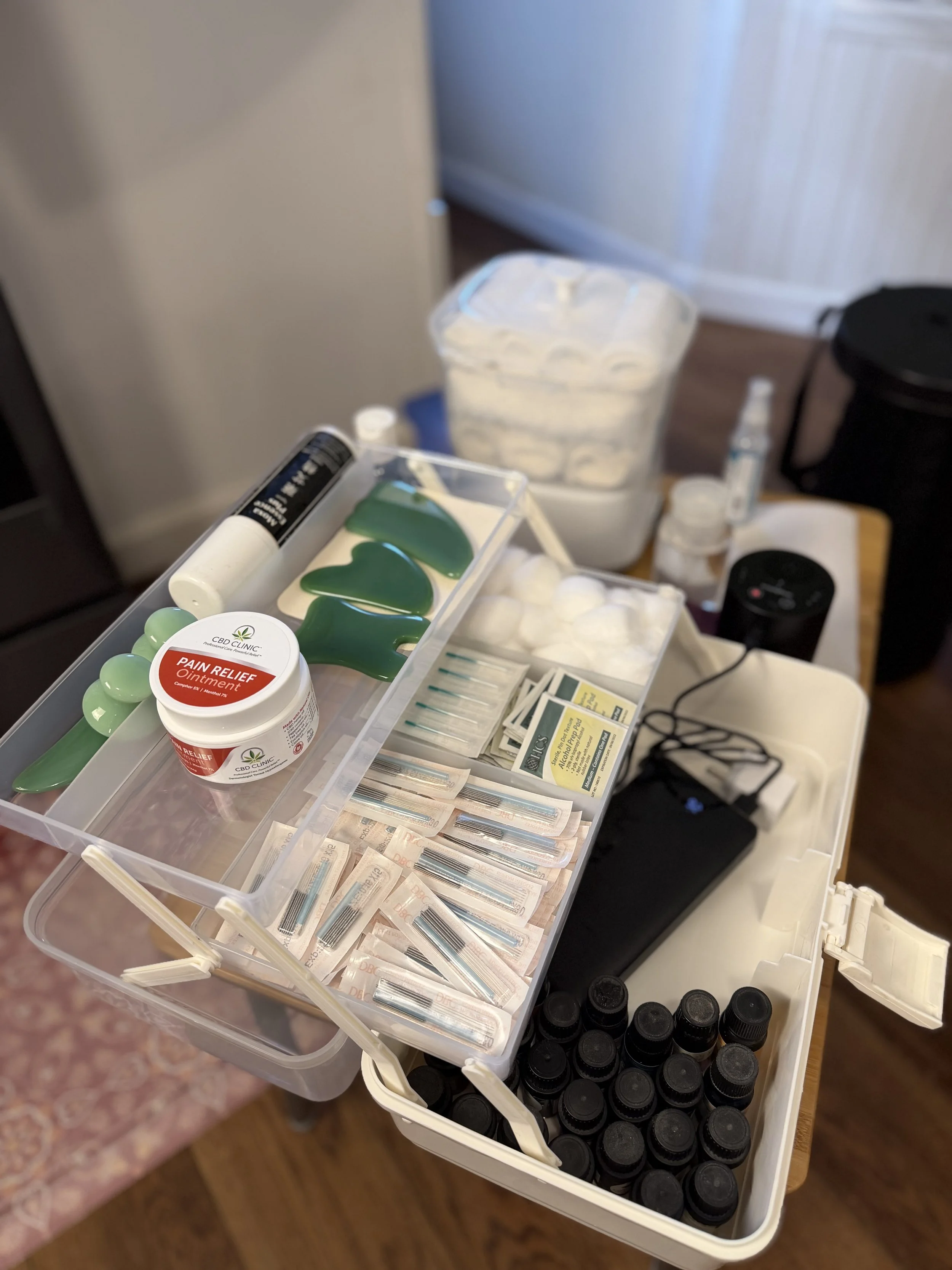 Medical supplies including syringes, CBD pain relief ointment, soap, vials of liquids, cotton balls, and small bottles on a plastic medical kit and a table.