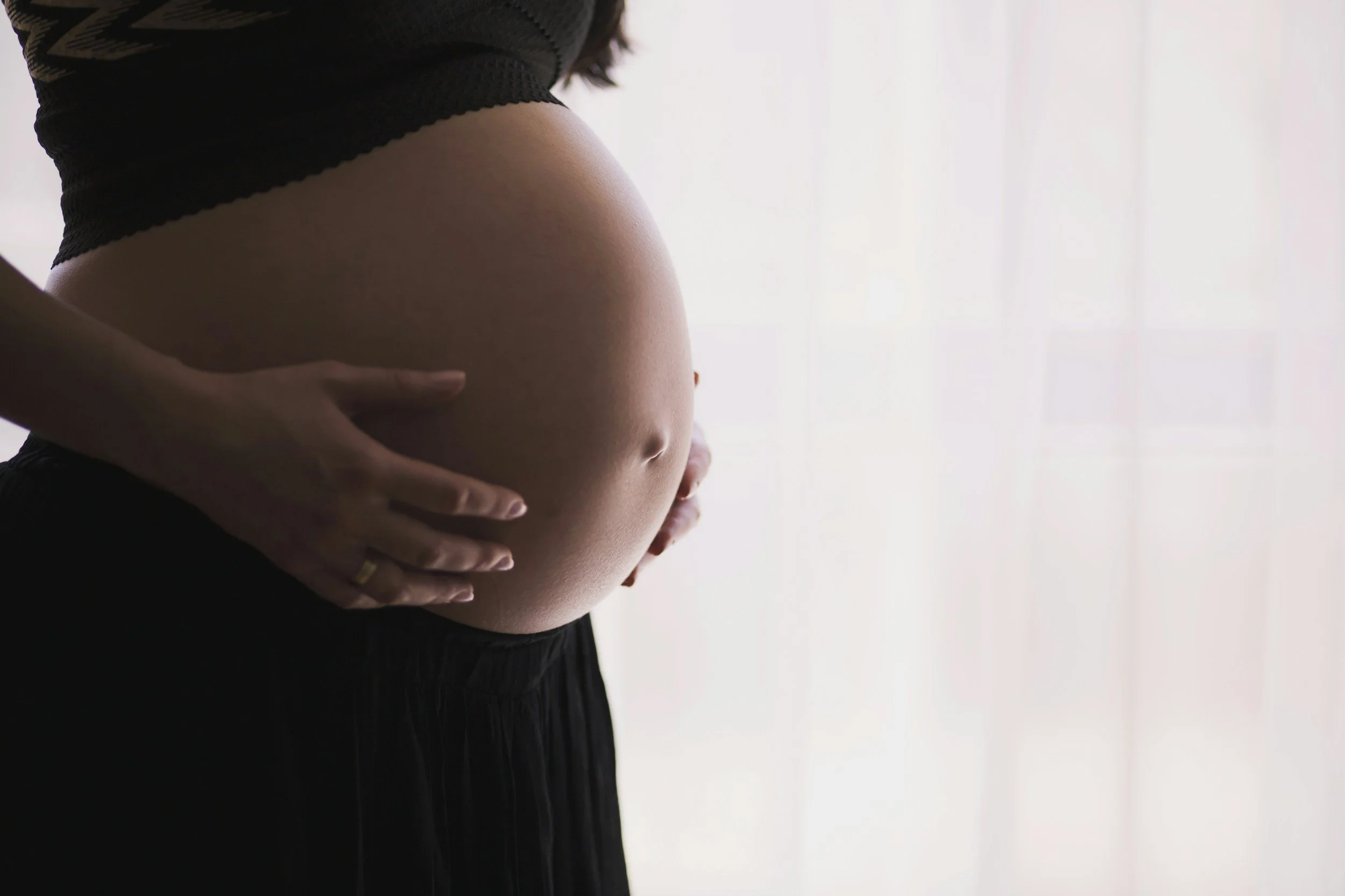 Close-up of a pregnant woman cradling her belly with both hands against a plain white background.