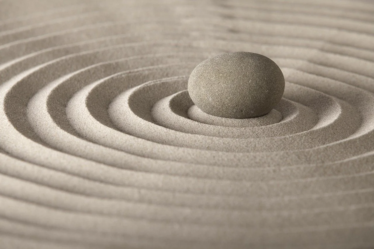A single round smooth stone placed on raked sand with concentric patterns.
