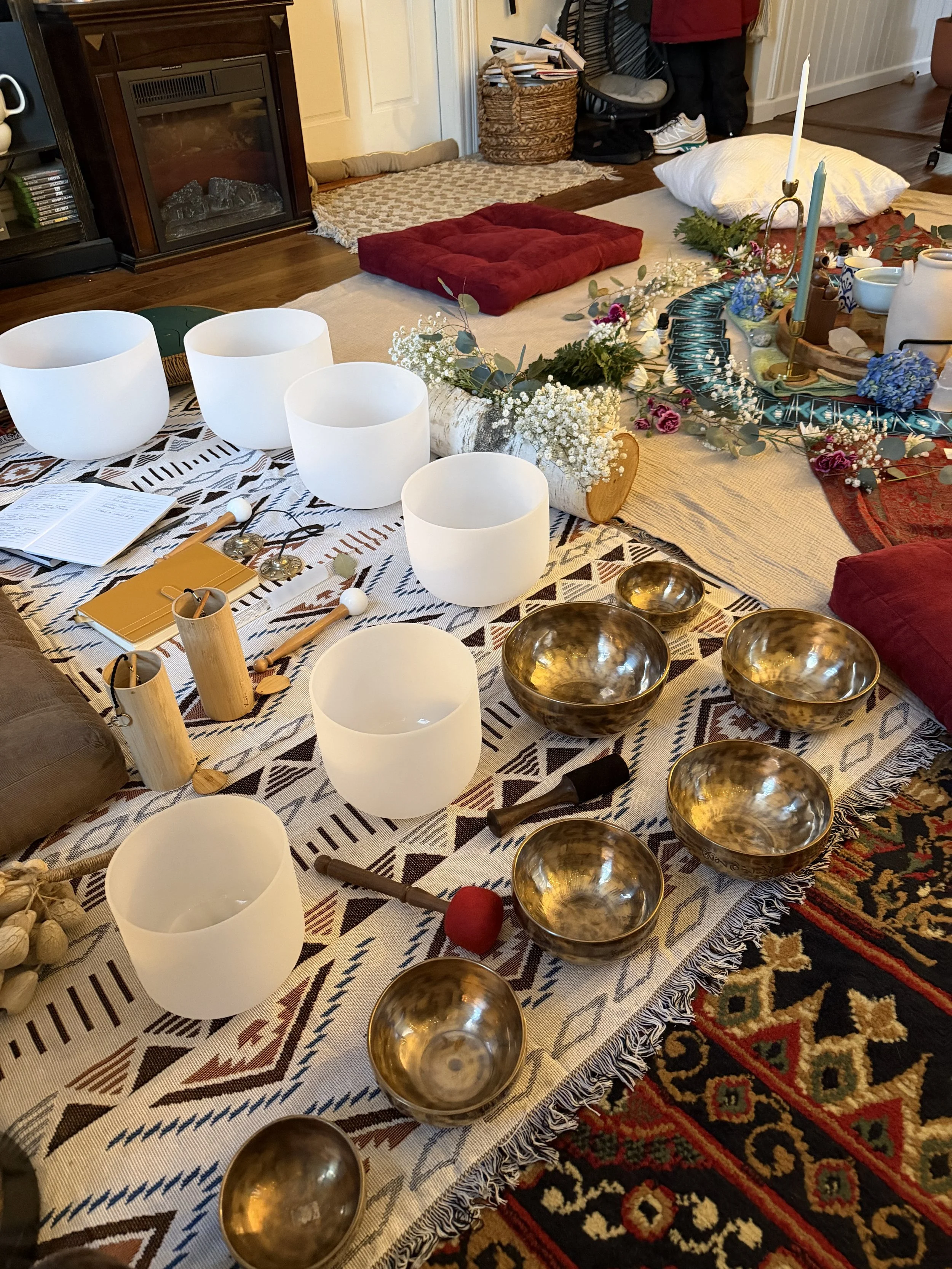 A person holding a brass singing bowl mallet above three brass singing bowls and a large brass bowl on a decorated surface.
