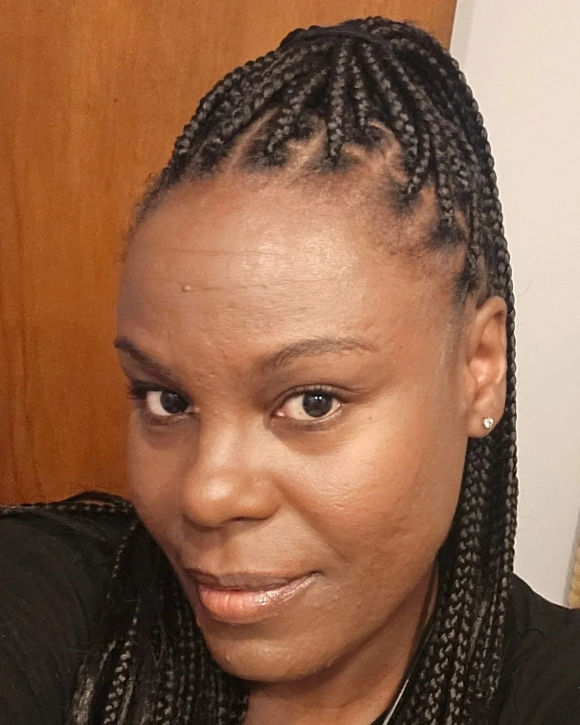 Close-up of woman with braids, earrings, and makeup, smiling at camera.