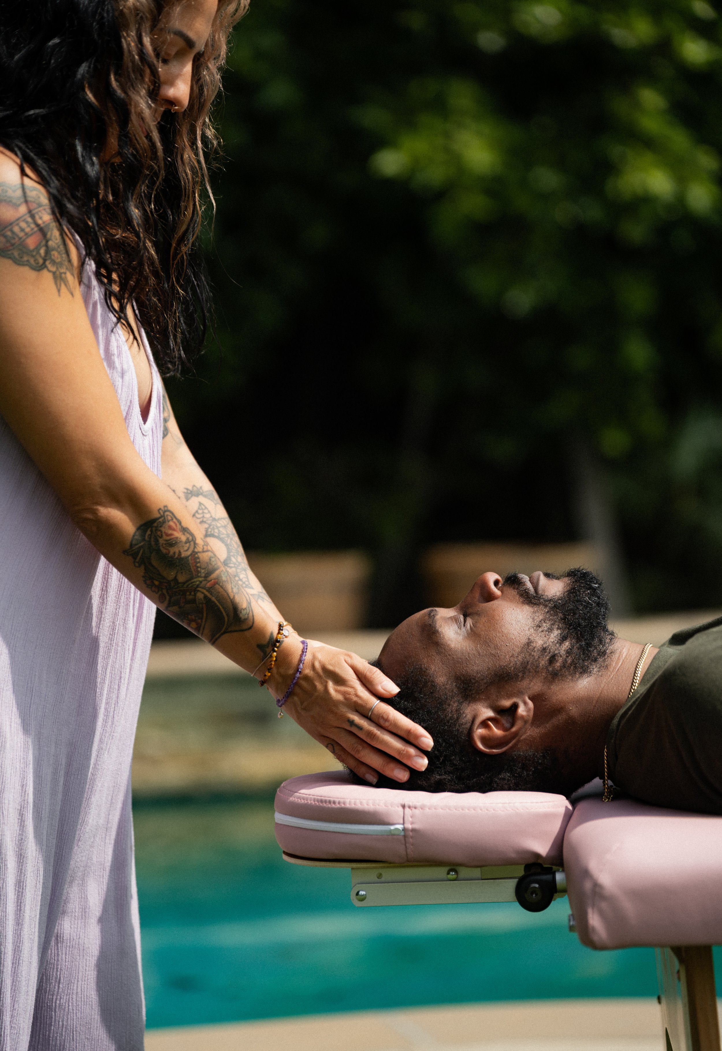 A woman giving a Reiki to a man lying face up on a massage table outdoors.