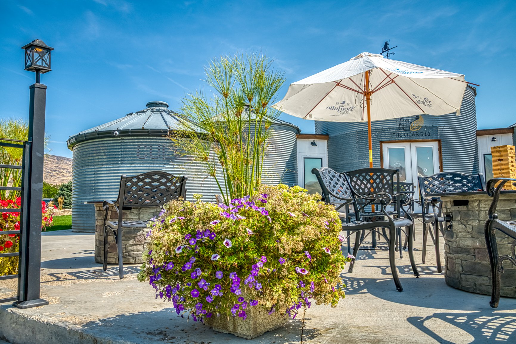 This photograph captures the distinctive character of Anderson Reserve Whiskey and Cigar Bar, where repurposed grain silos and refined outdoor seating create a unique blend of rustic Idaho heritage and modern hospitality. Bright flowers, clean lines,
