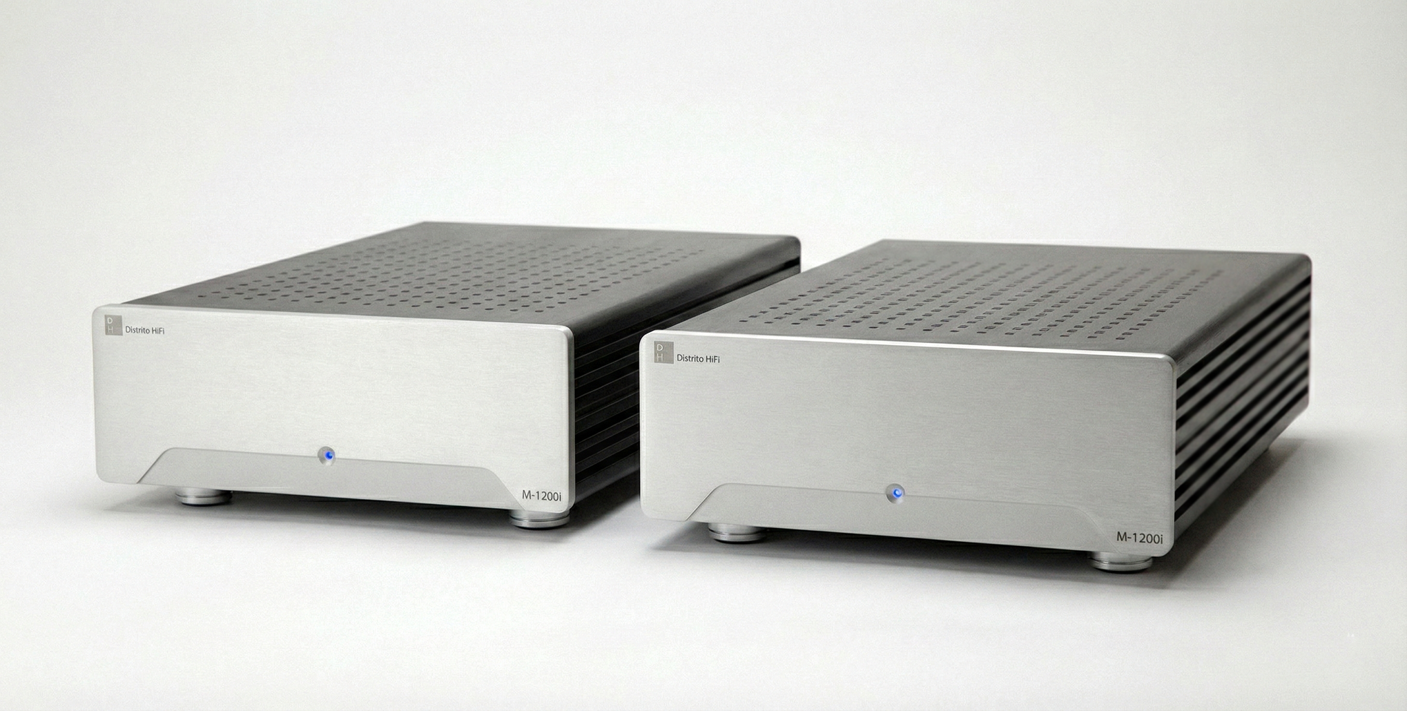 Dos amplificadores de audio en color plateado con perforaciones en la parte superior y una pequeña luz azul en la parte frontal.