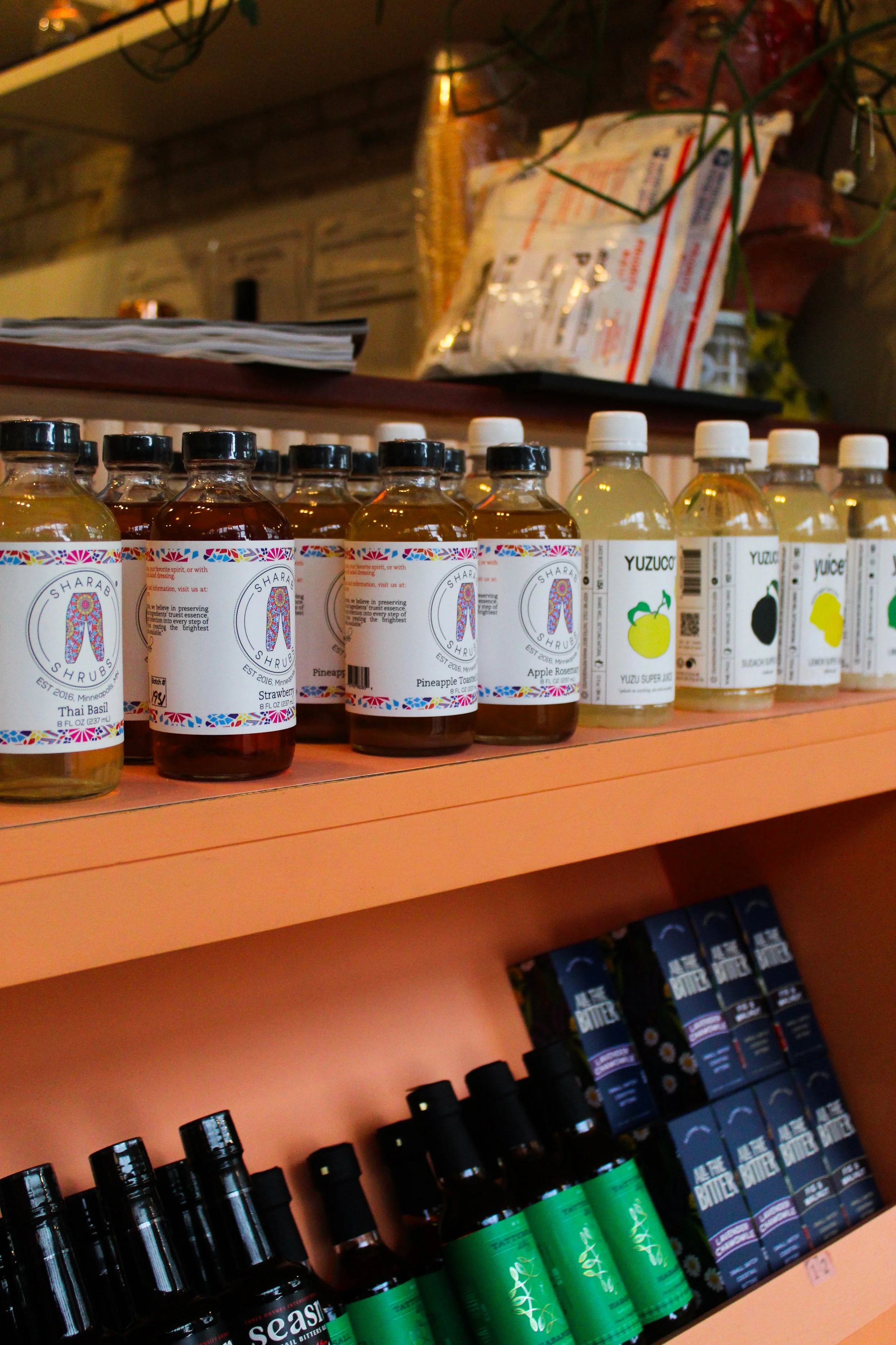 Shelf displaying bottles of herbal and plant-based products such as facial sprays and extracts, with some packaged items and a blurred background of additional products. photo by Atika Goble branding and product photographer in minneapolis atikagoble