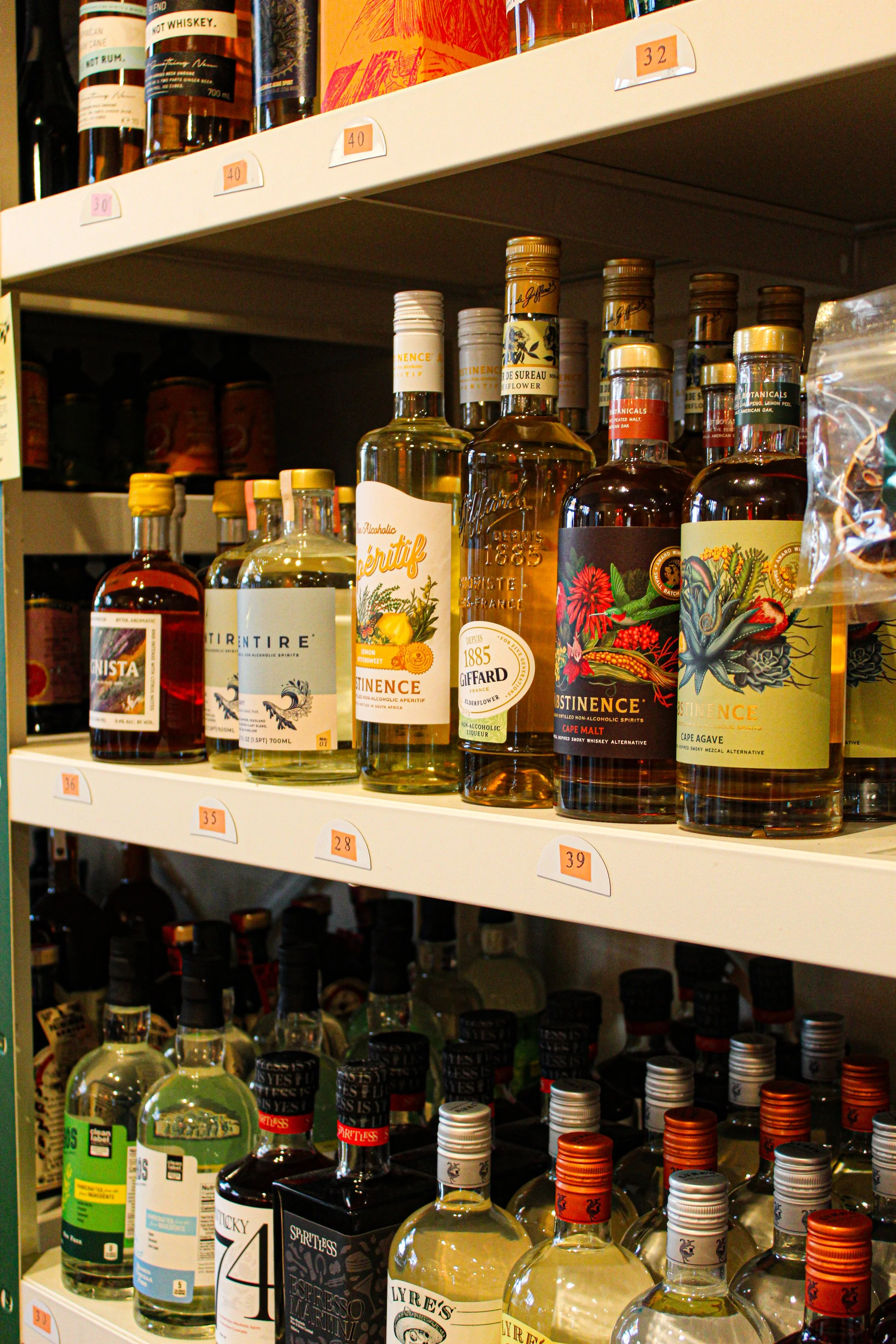 Shelf with various bottles of alcohol, including non alcoholic whiskey and spirits, organized with labeled price tags. photo by Atika Goble branding and product photographer in minneapolis atikagoble.com