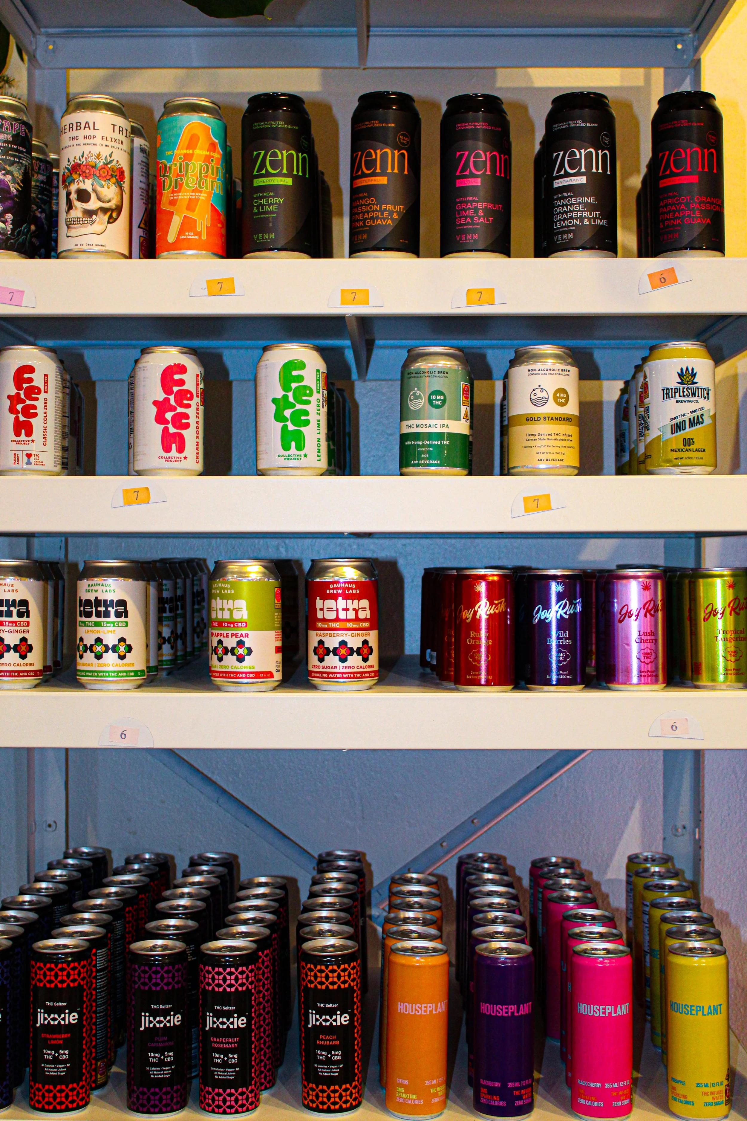 Shelf with various canned and bottled beverages, including THC-infused drinks, sparkling waters, and energy drinks, with colorful labels and some price labels. marigold bottle shop photo by Atika Goble branding and product photographer in minneapolis
