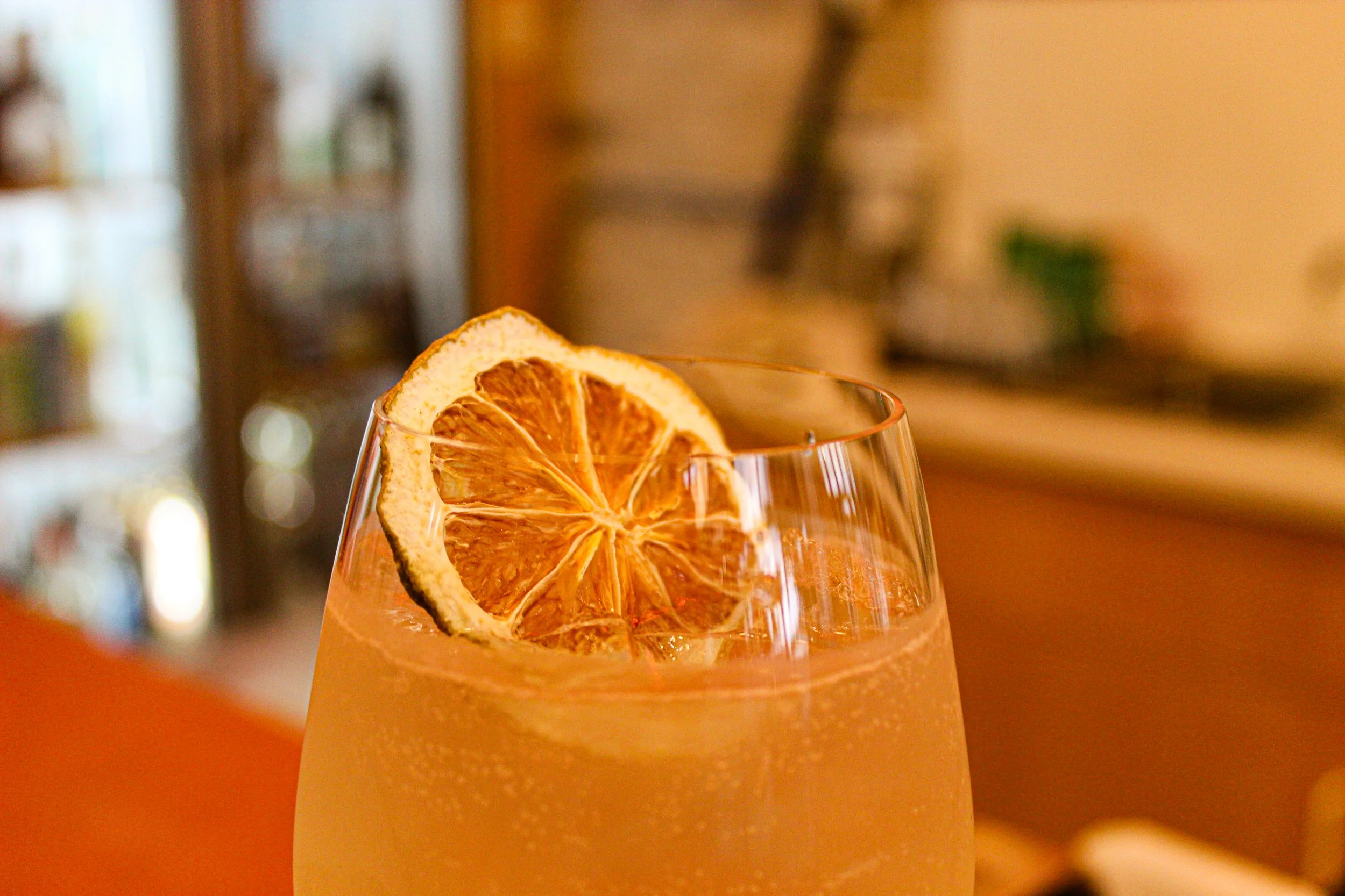 Close-up of a glass with an orange-colored drink garnished with dried orange slices. photo by Atika Goble branding and product photographer in minneapolis atikagoble.com