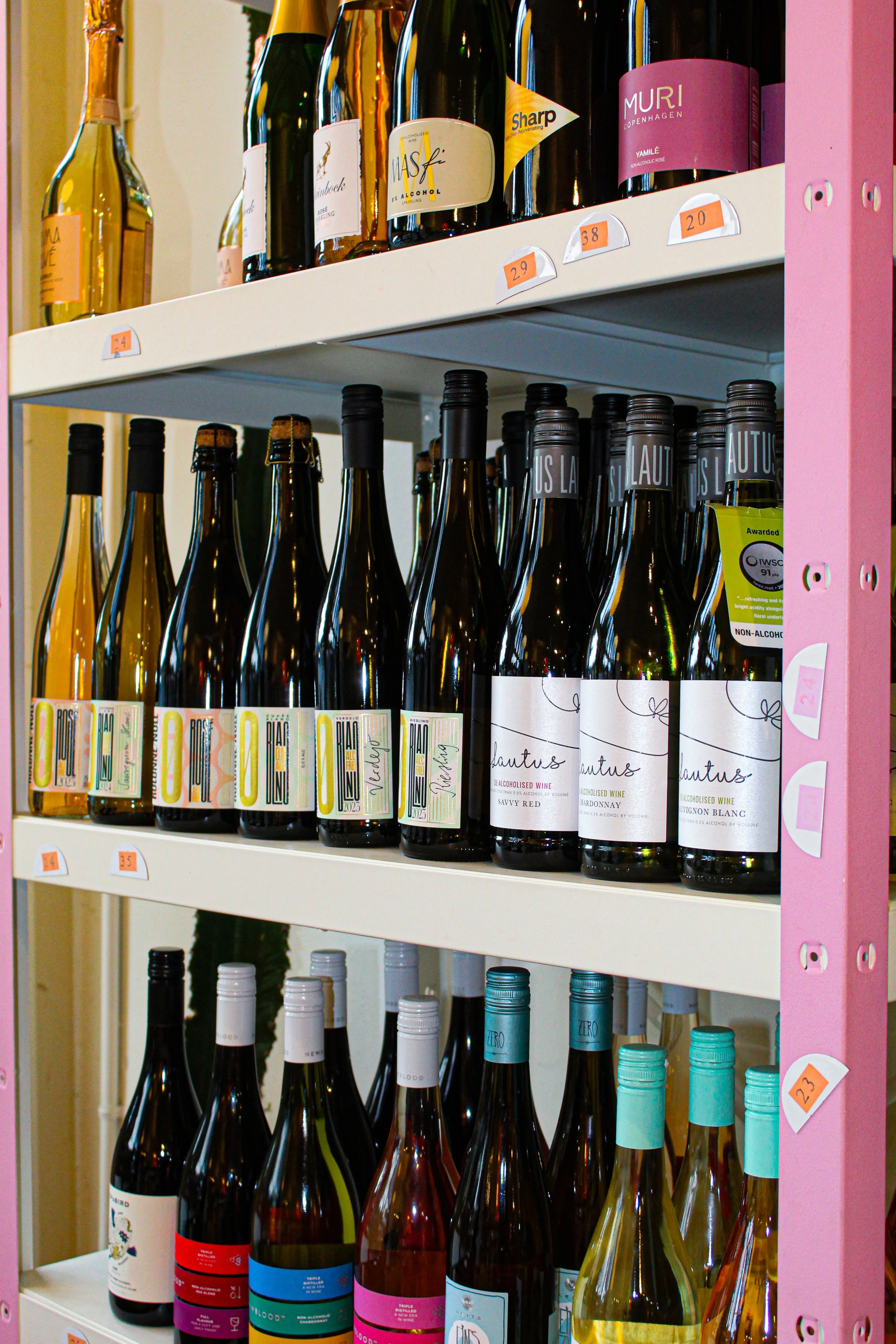 Shelf with various bottles of alcohol, including wine and spirits, organized in rows with price tags attached. Some bottles have colorful labels and caps. marigold minneapolis bottle shop photo by Atika Goble branding and product photographer in minn