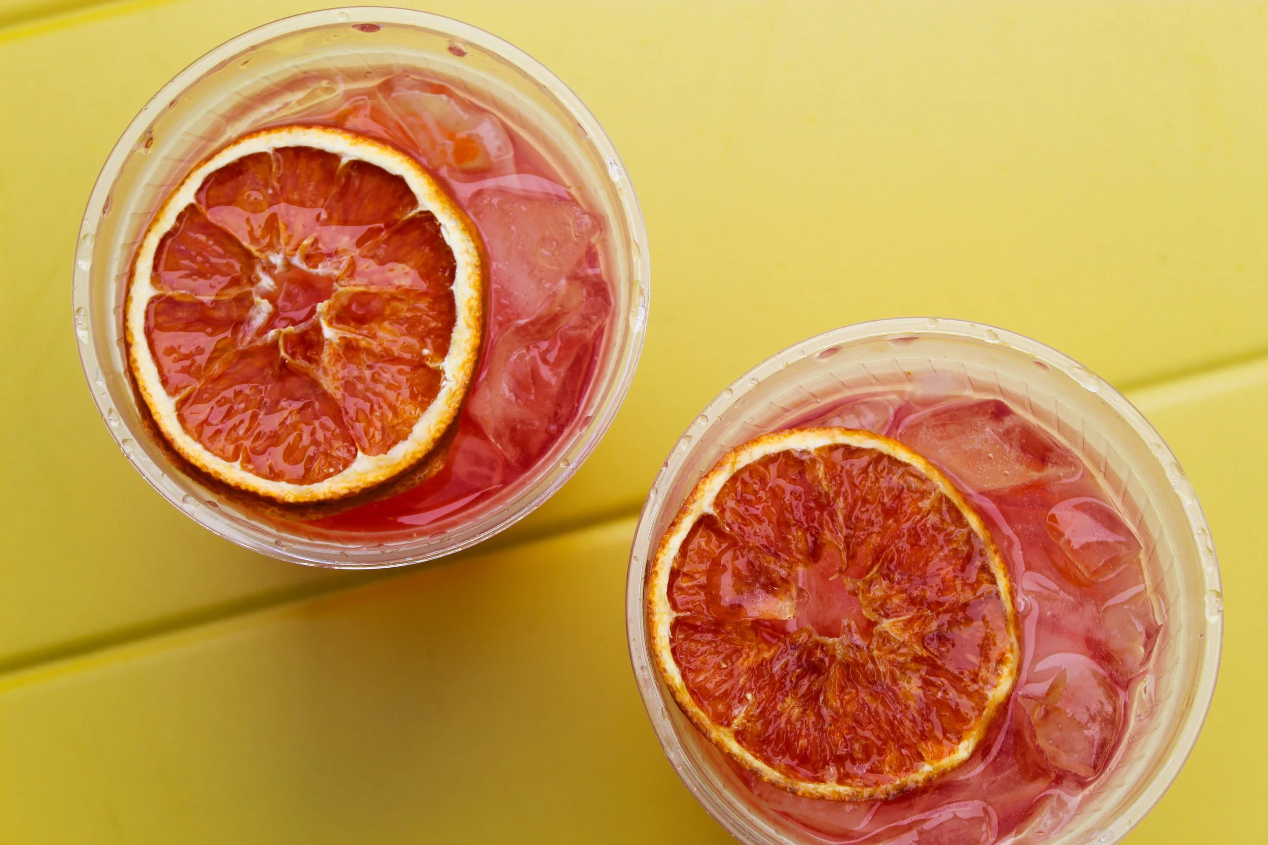 Close-up of two cups containing sliced oranges and ice, on a yellow surface.