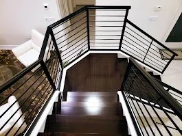 Top view of a staircase with dark wood steps and black metal railings, leading down to a landing.