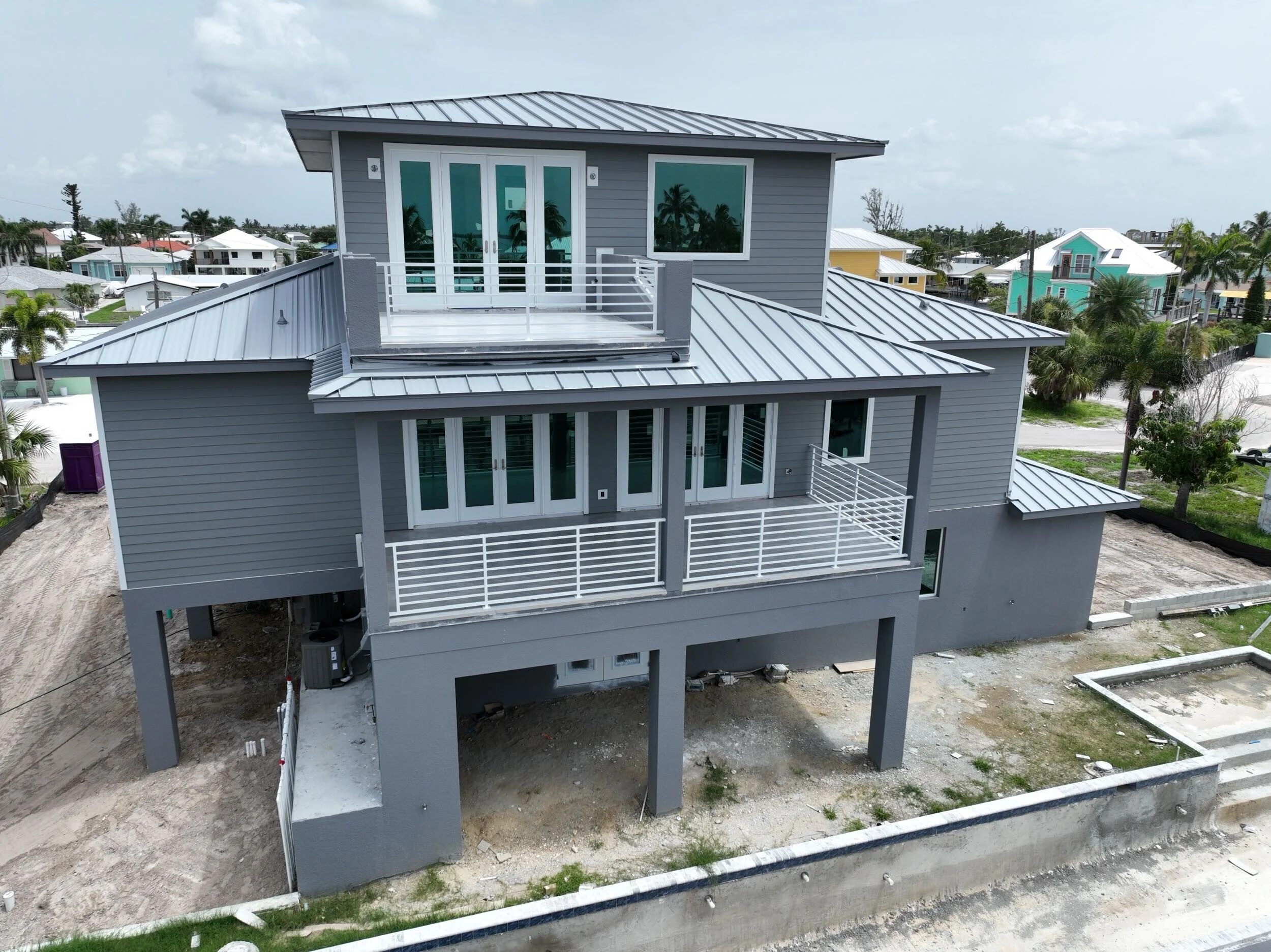 New gray multi-story with custom balcony railing and metal roof nearby colorful houses.