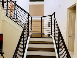Indoor staircase with black metal railing leading to an upper level, beige walls, and closed door at the top.