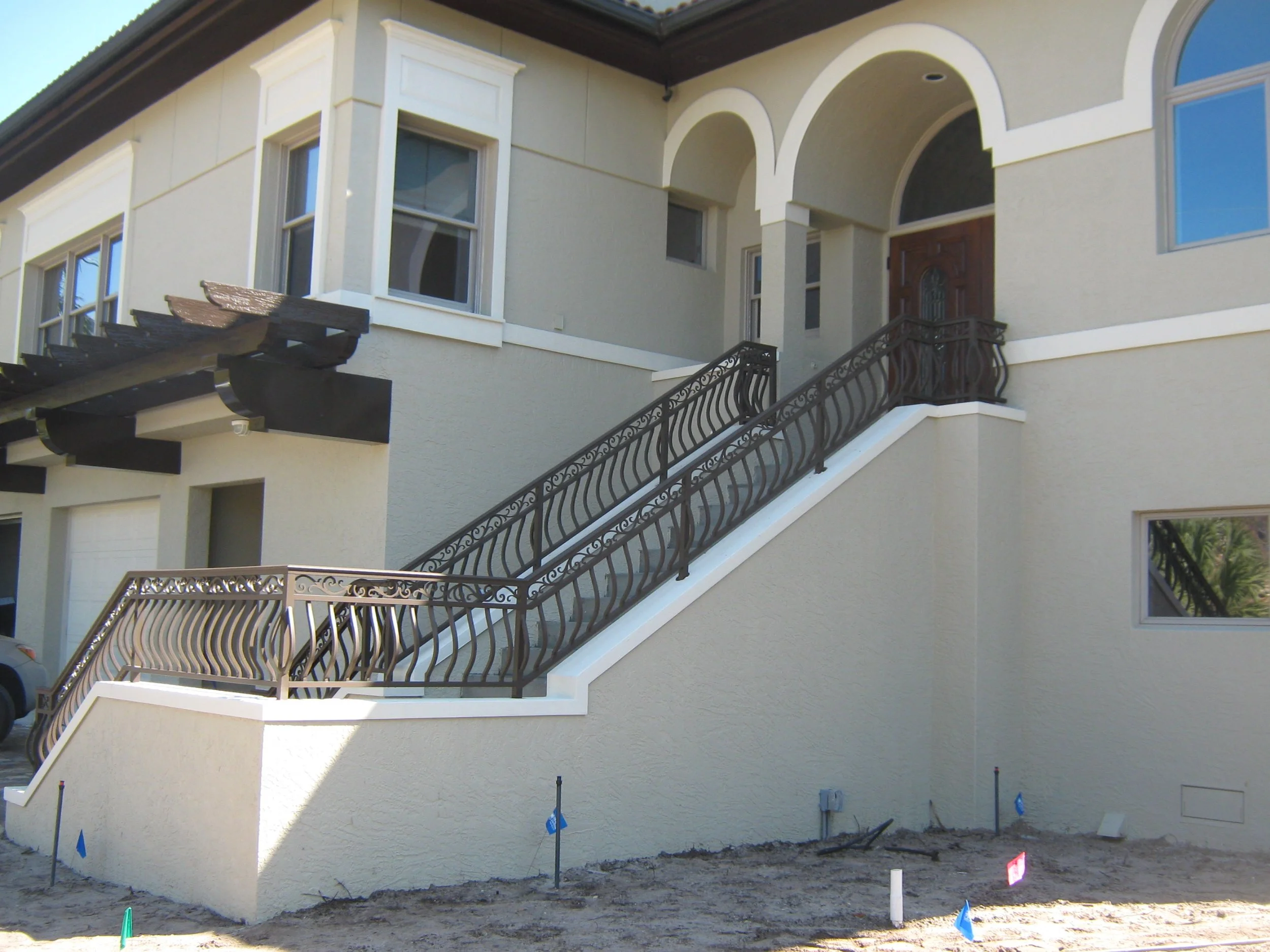 Newly constructed beige house with decorative staircase leading to front door, multiple windows, and ongoing landscaping at the front yard.