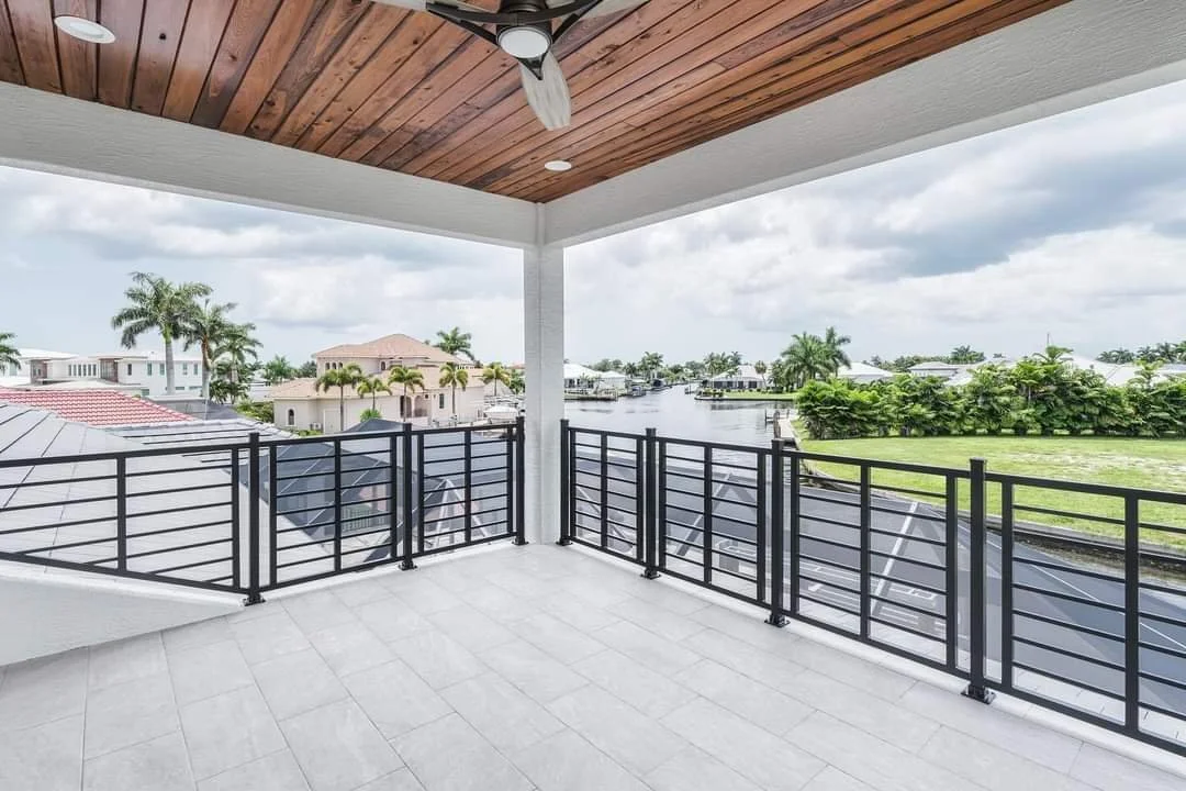 View from a balcony with custom ornate aluminum railing, waterway, and palm trees, with a wooden ceiling, ceiling fan, and white tiled floor.