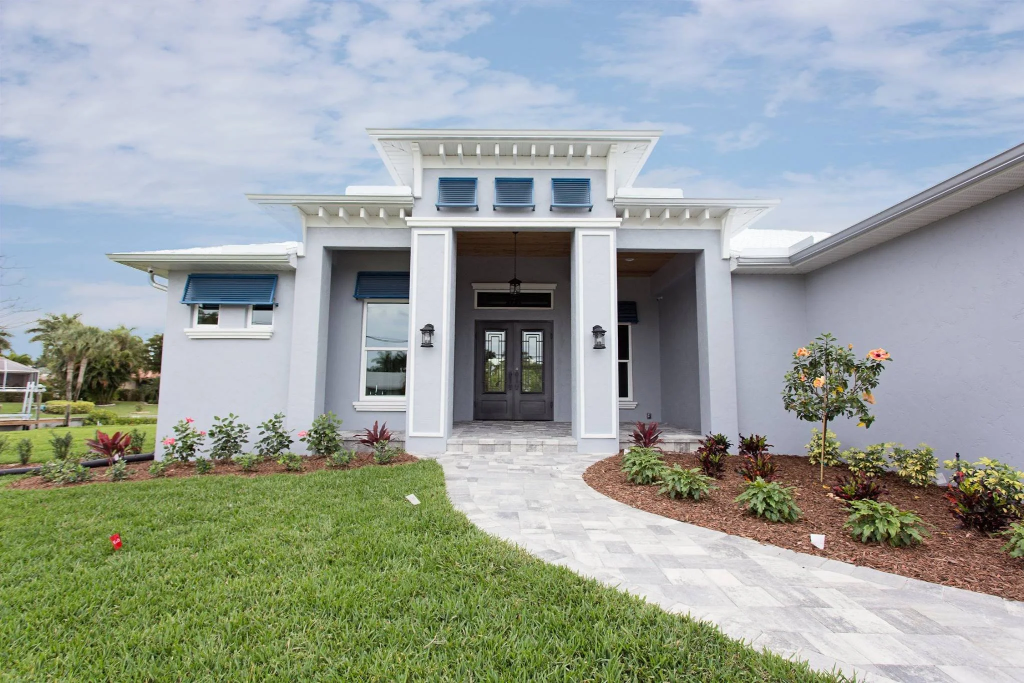 Modern white house with dark front door, landscaped front yard, and blue shutters and deco grills on windows, under partly cloudy sky.