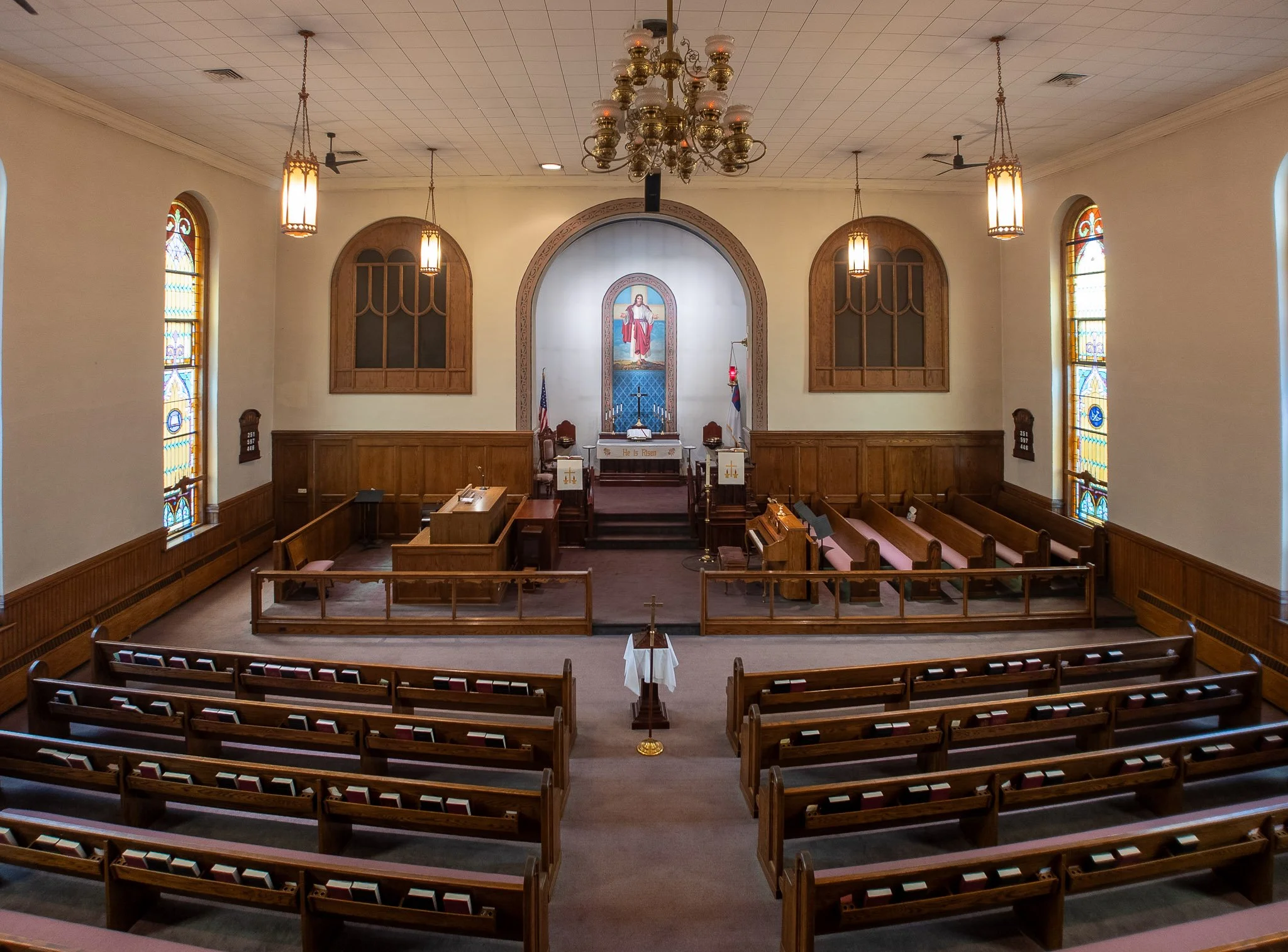 Interior of a church sanctuary with wooden pews, an altar, stained glass windows, and religious icons.