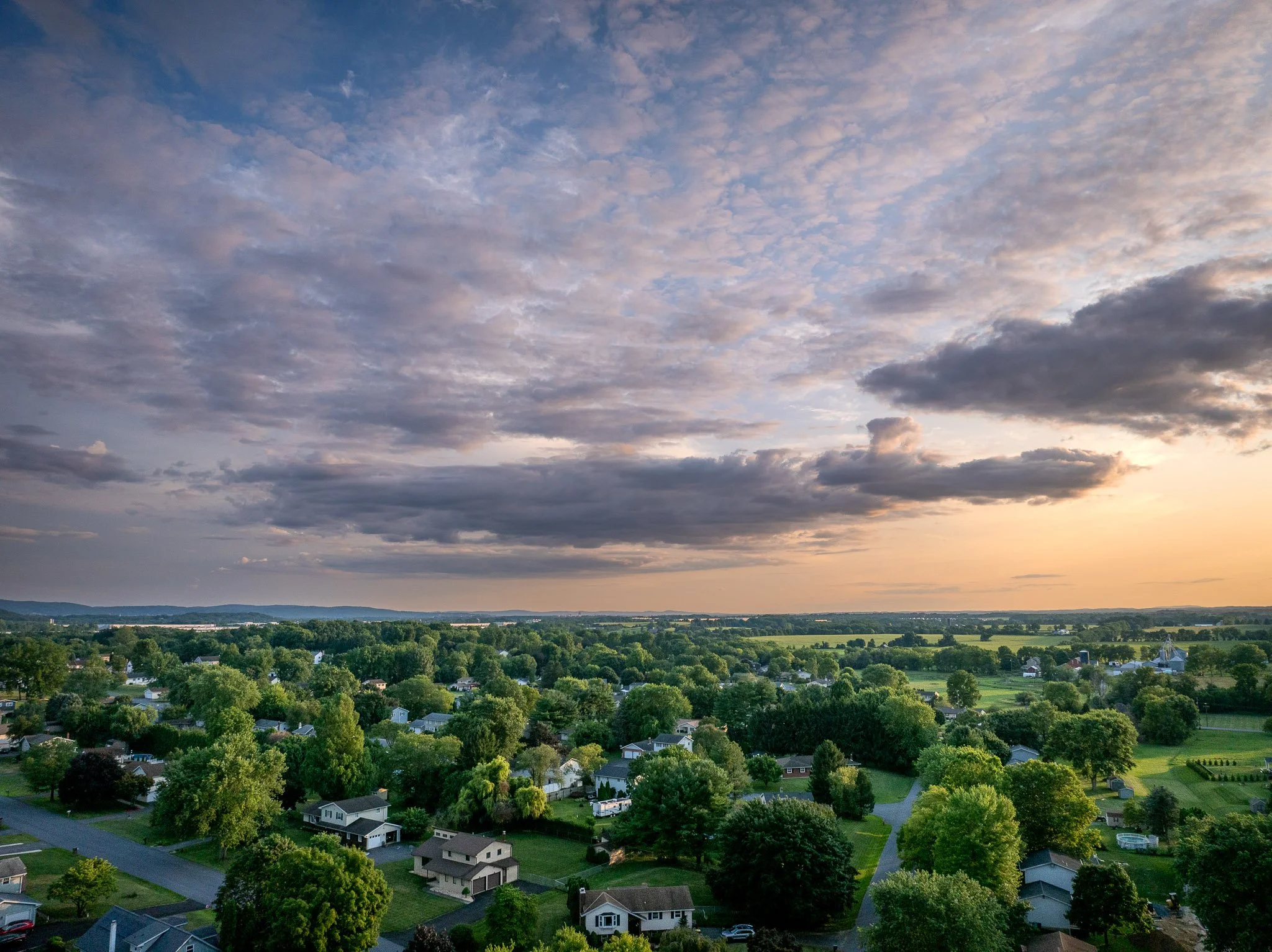 Aerial view of a suburban Nazareth neighborhood with houses and green trees, under a partly cloudy sky at sunset.