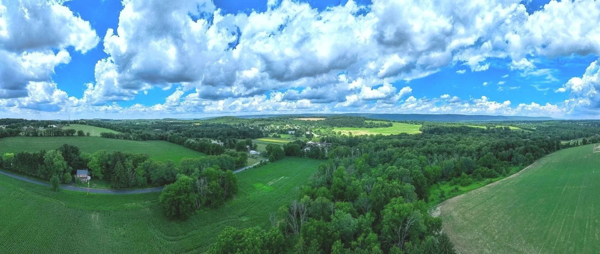 A panoramic aerial view of lush green farmland and forests under a partly cloudy sky near Moorestown, PA.