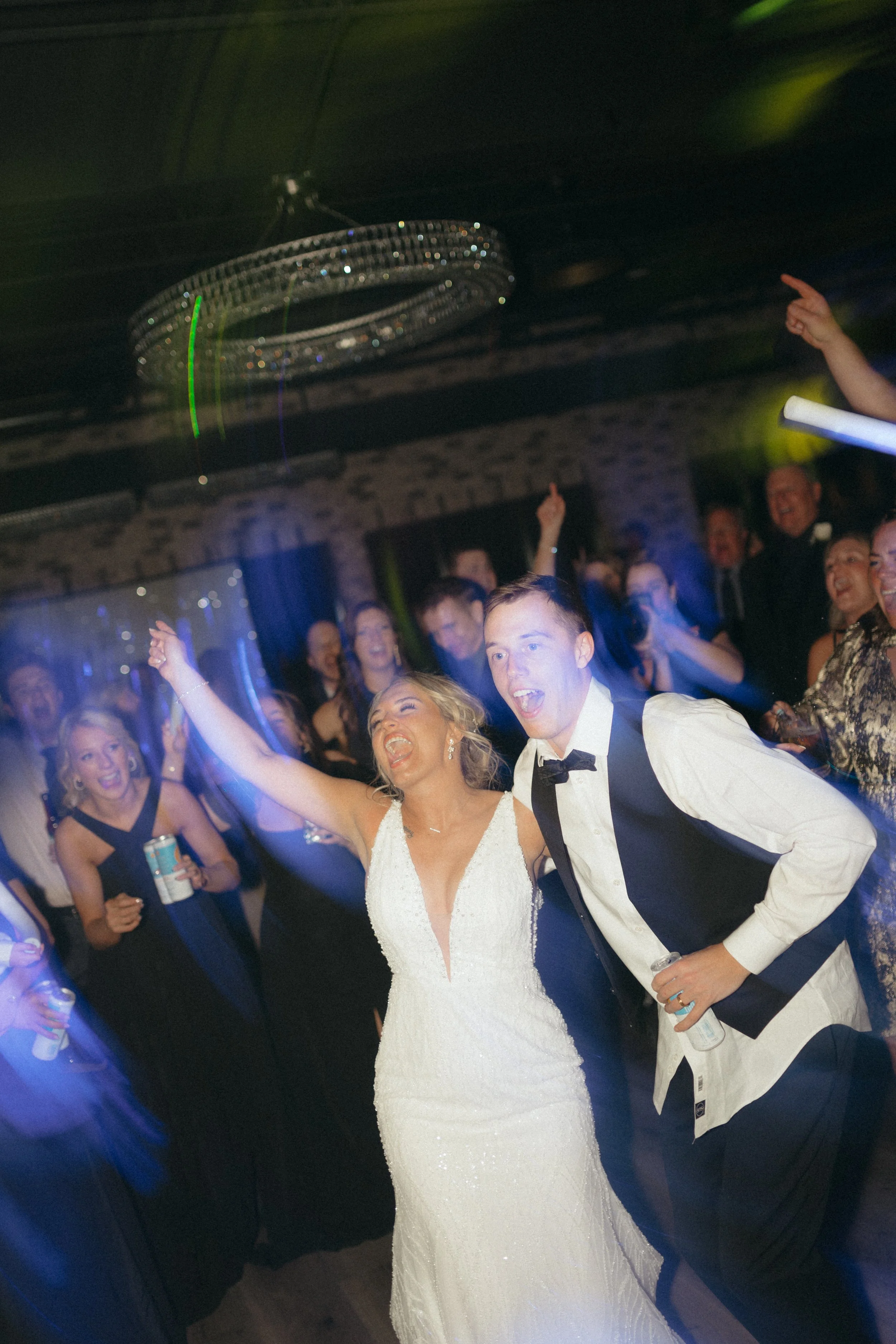 Bride and groom celebrating on dance floor with guests in evening attire at a wedding reception.