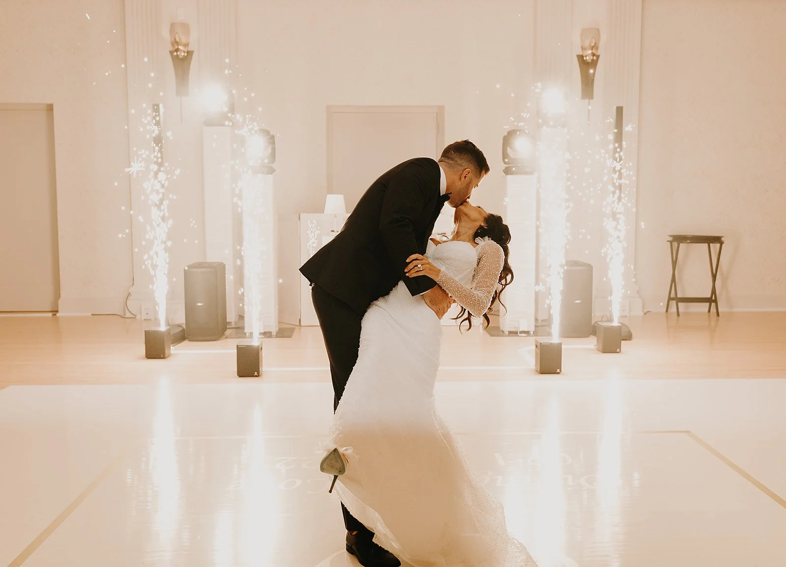Bride and groom kissing on wedding dance floor with sparklers.