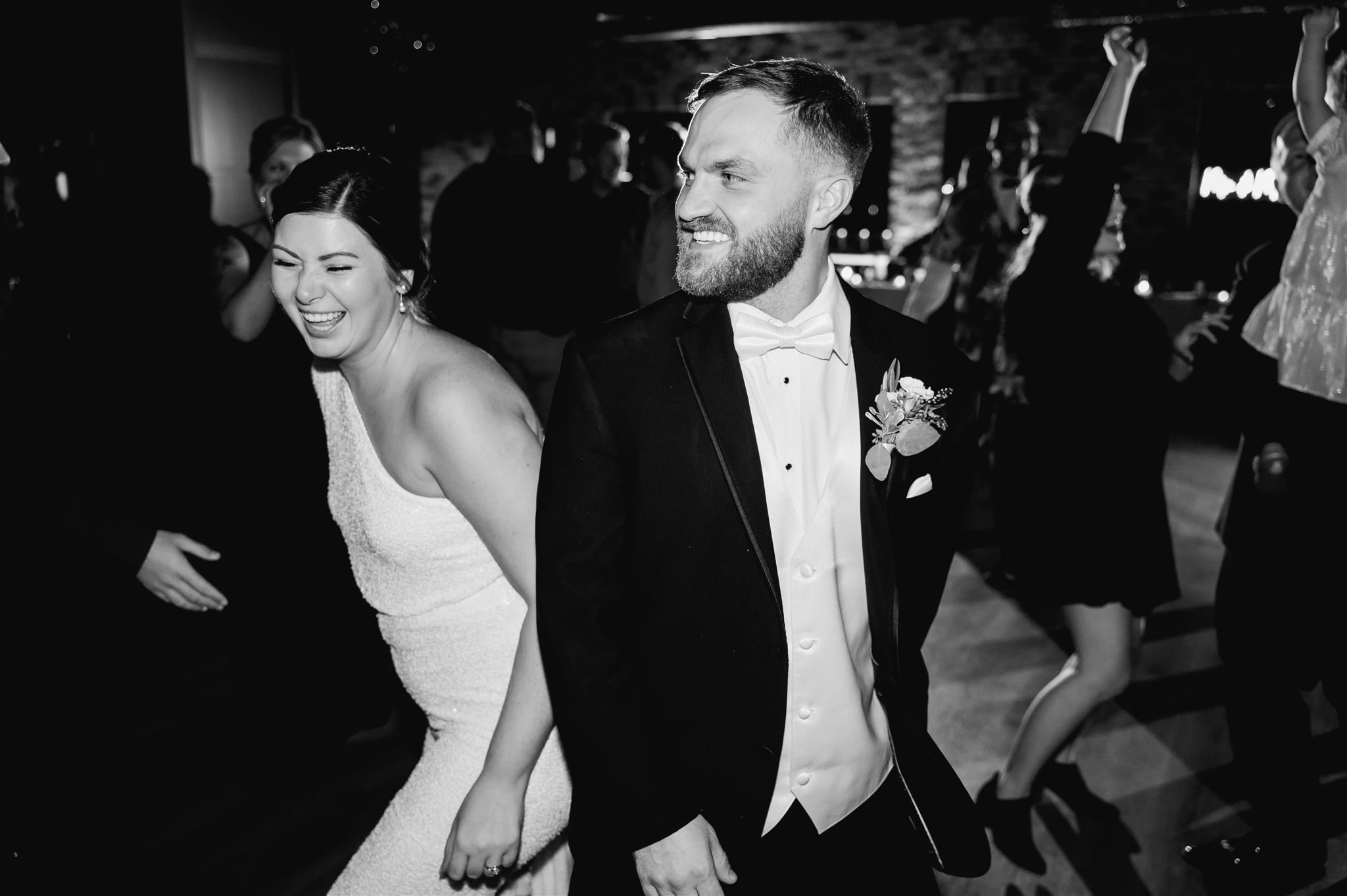 Bride and groom dancing at a wedding reception with guests celebrating around them.