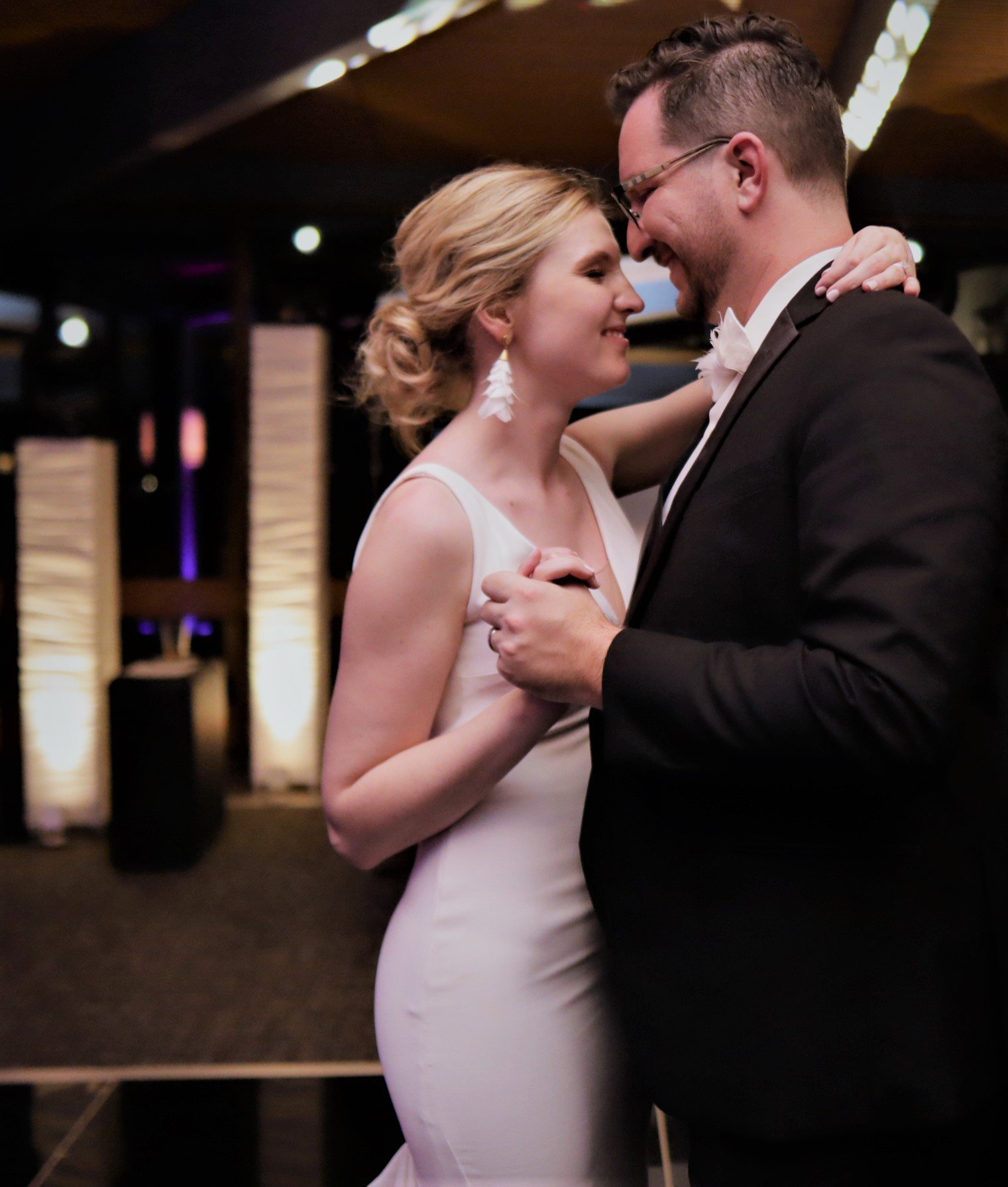 A couple dancing closely at a wedding reception, with the woman wearing a white dress and the man in a black tuxedo.