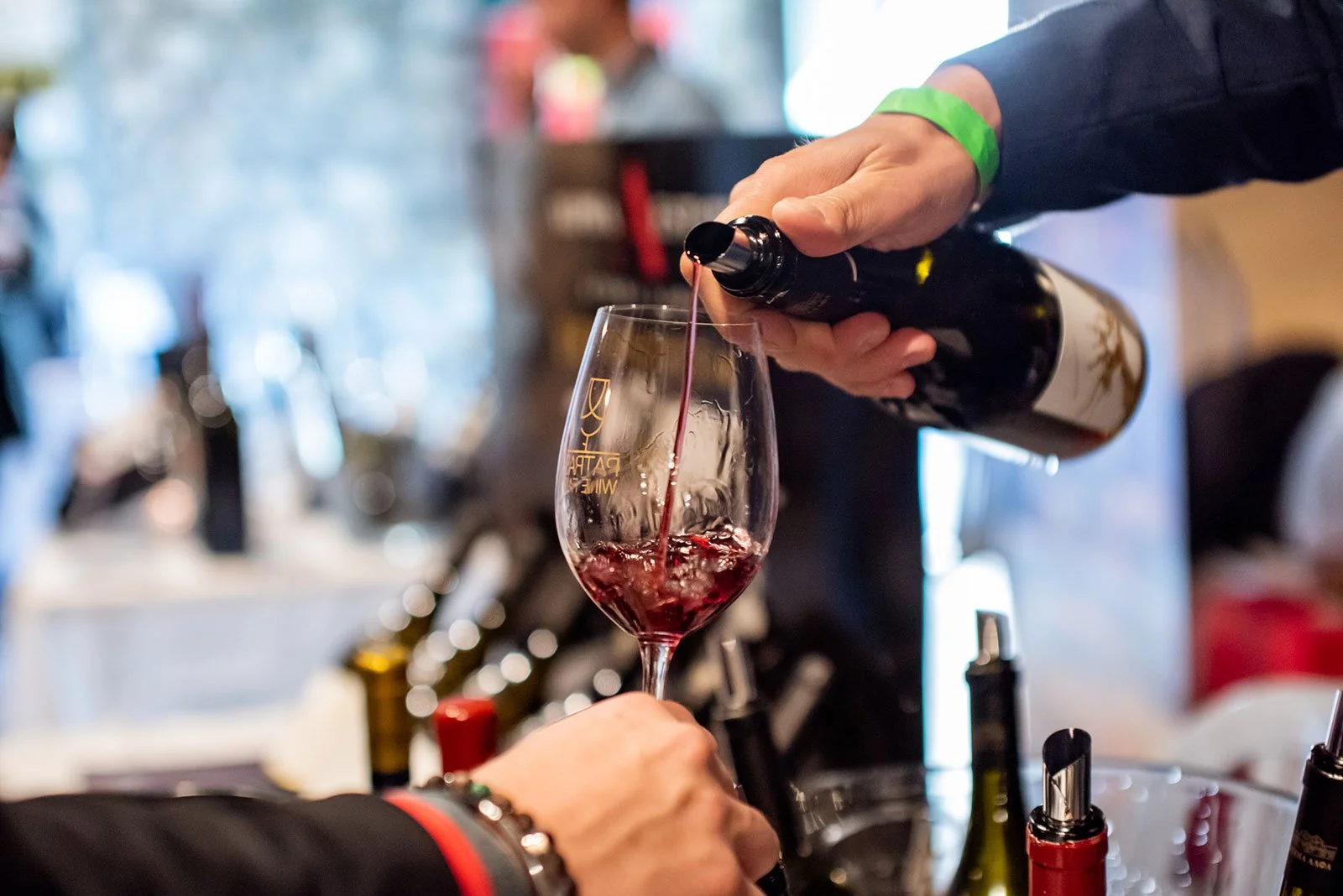 Person pouring red wine into a wine glass at a tasting event.