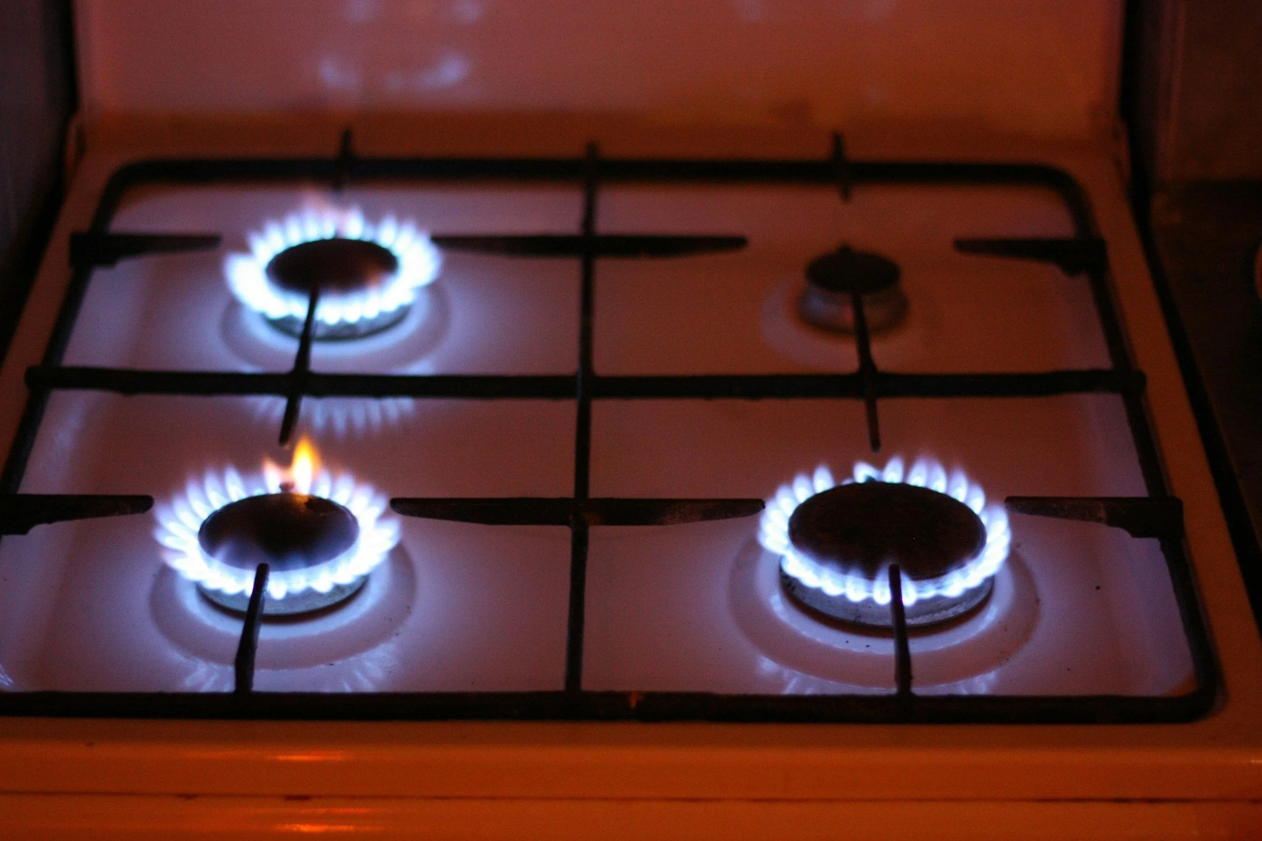 Four blue-flamed burners on a white gas stove, with two burners on and two off.