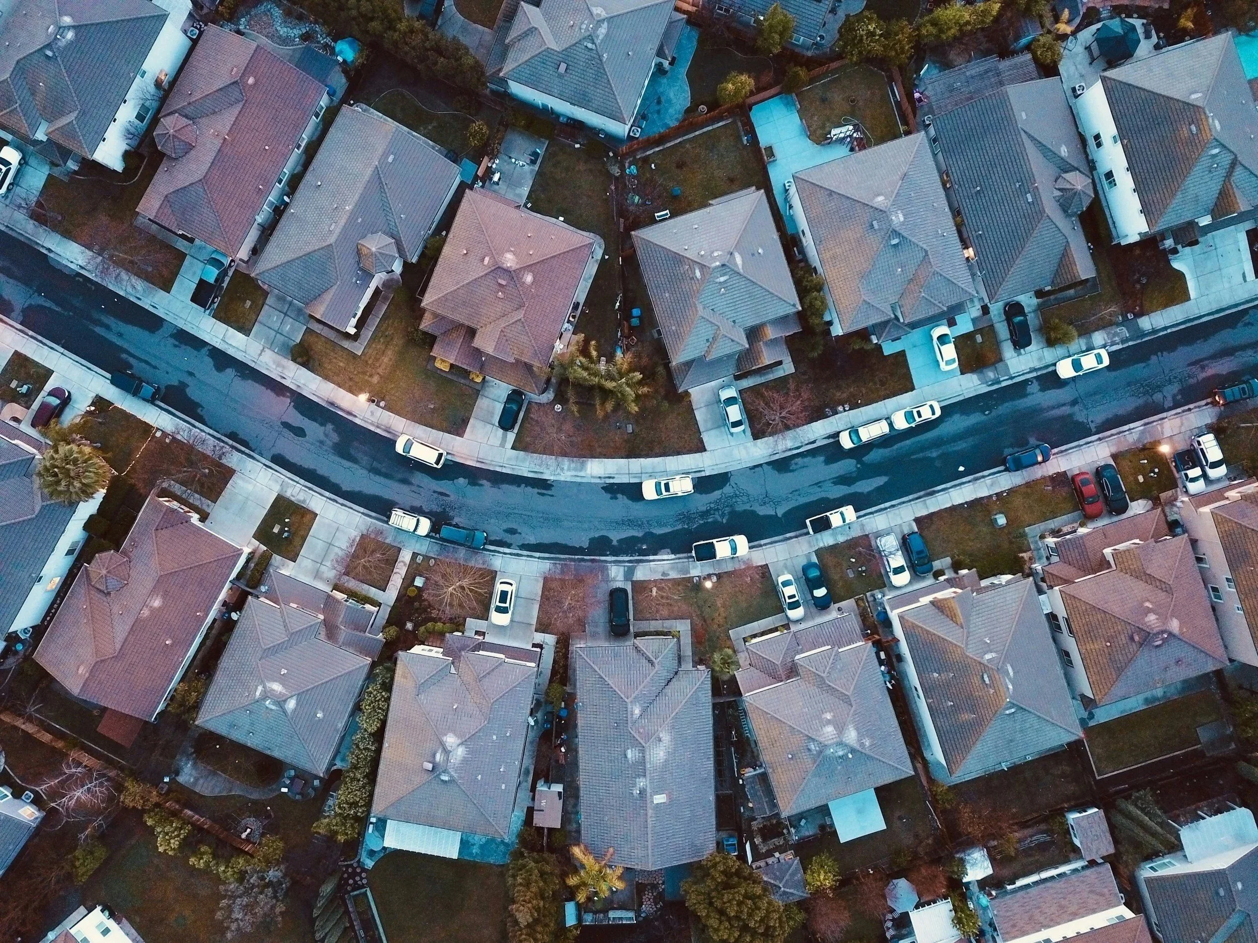 An aerial view of a suburban neighborhood showing houses, parked cars along the curb, and a curved street in Sacramento County