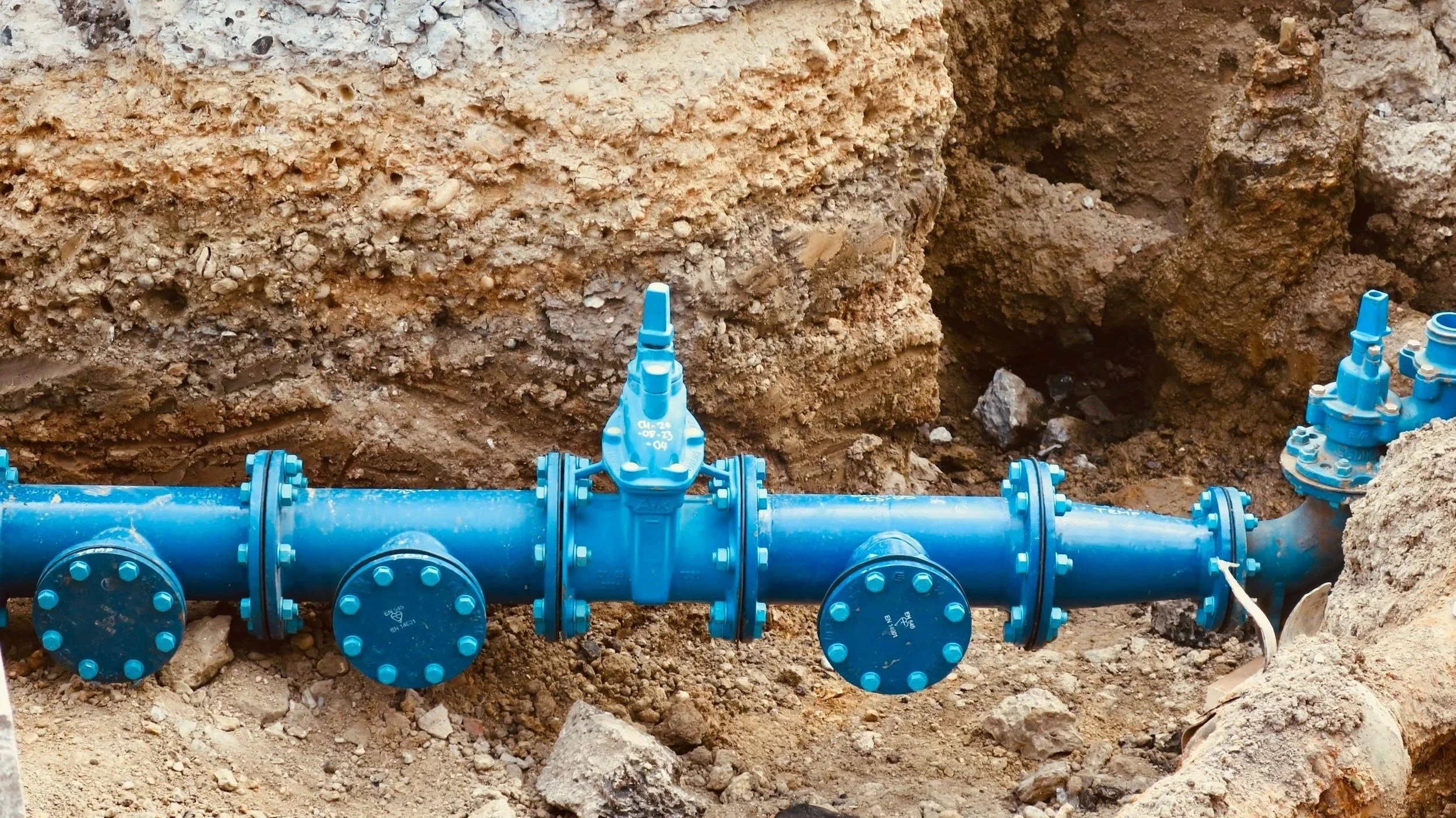 Blue underground water pipe with valves buried in dirt at a construction site for repiping service.