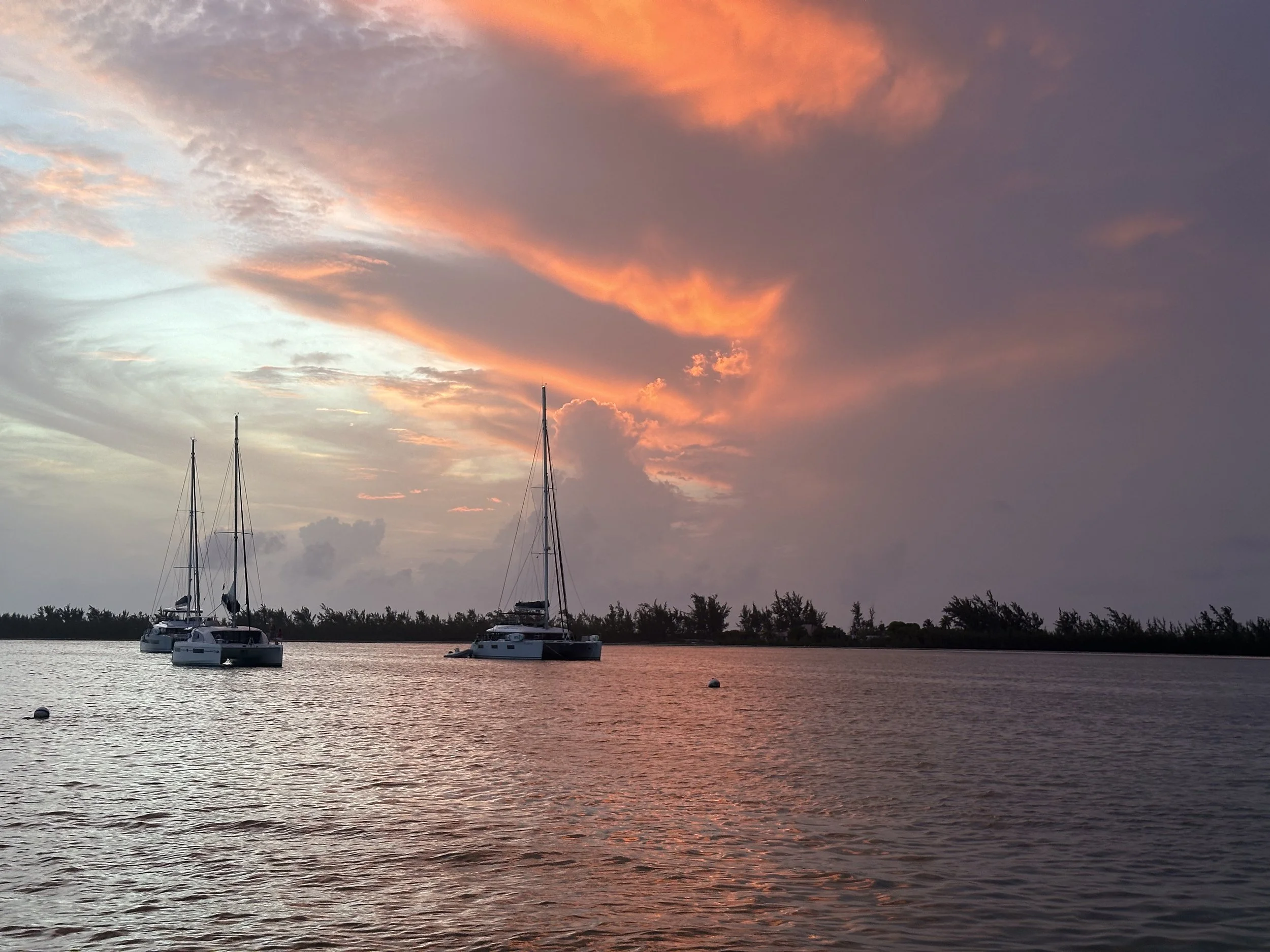 Sailboats floating on calm water at sunset, with a colorful sky filled with pink and orange clouds.